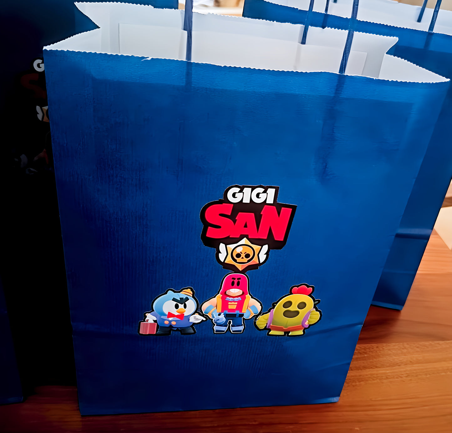 Blue gift bag with Gigi San logo and three cartoon characters on a wooden table