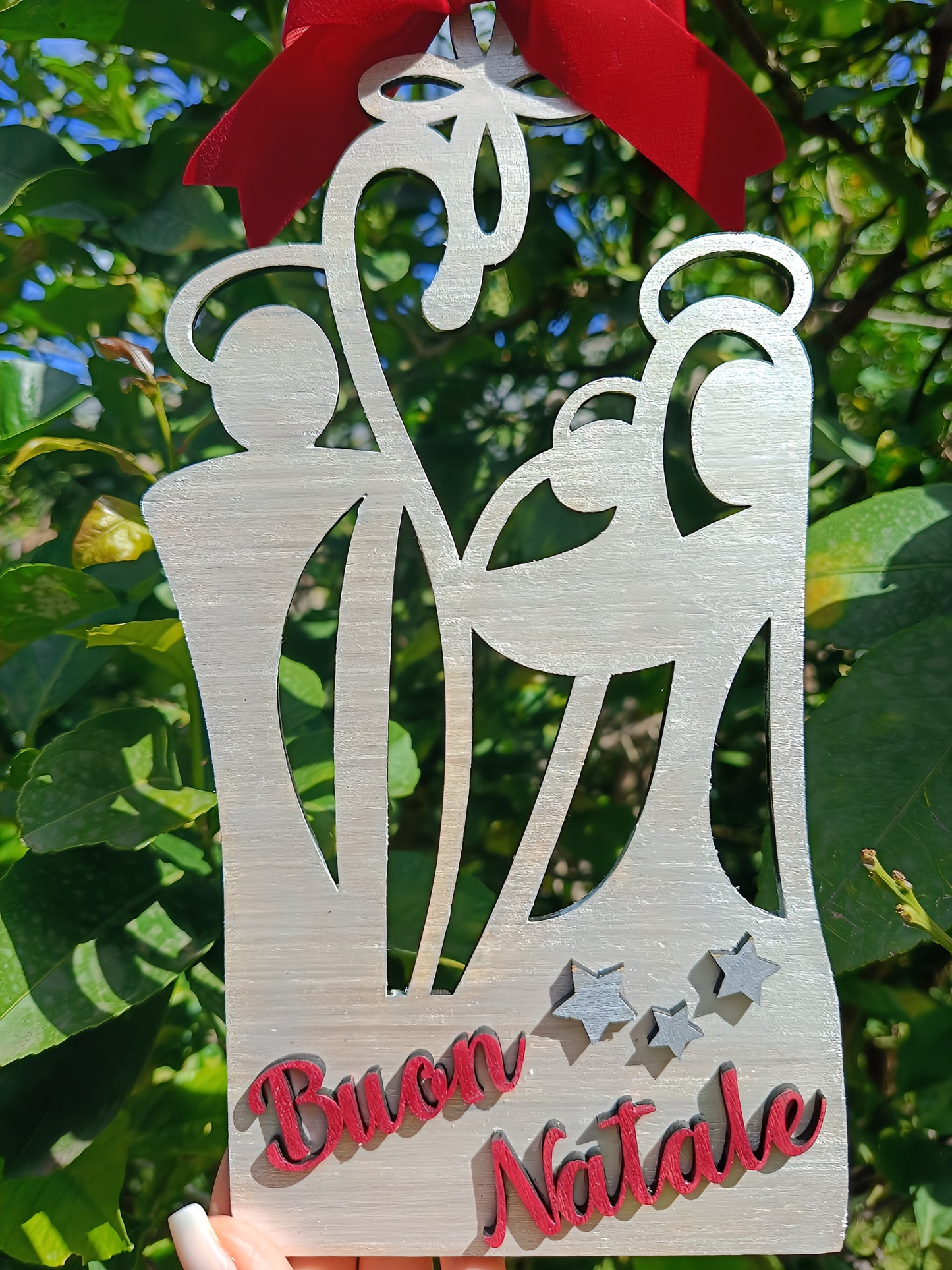 Wooden Christmas ornament with nativity scene, Buon Natale text, red bow, outdoor setting