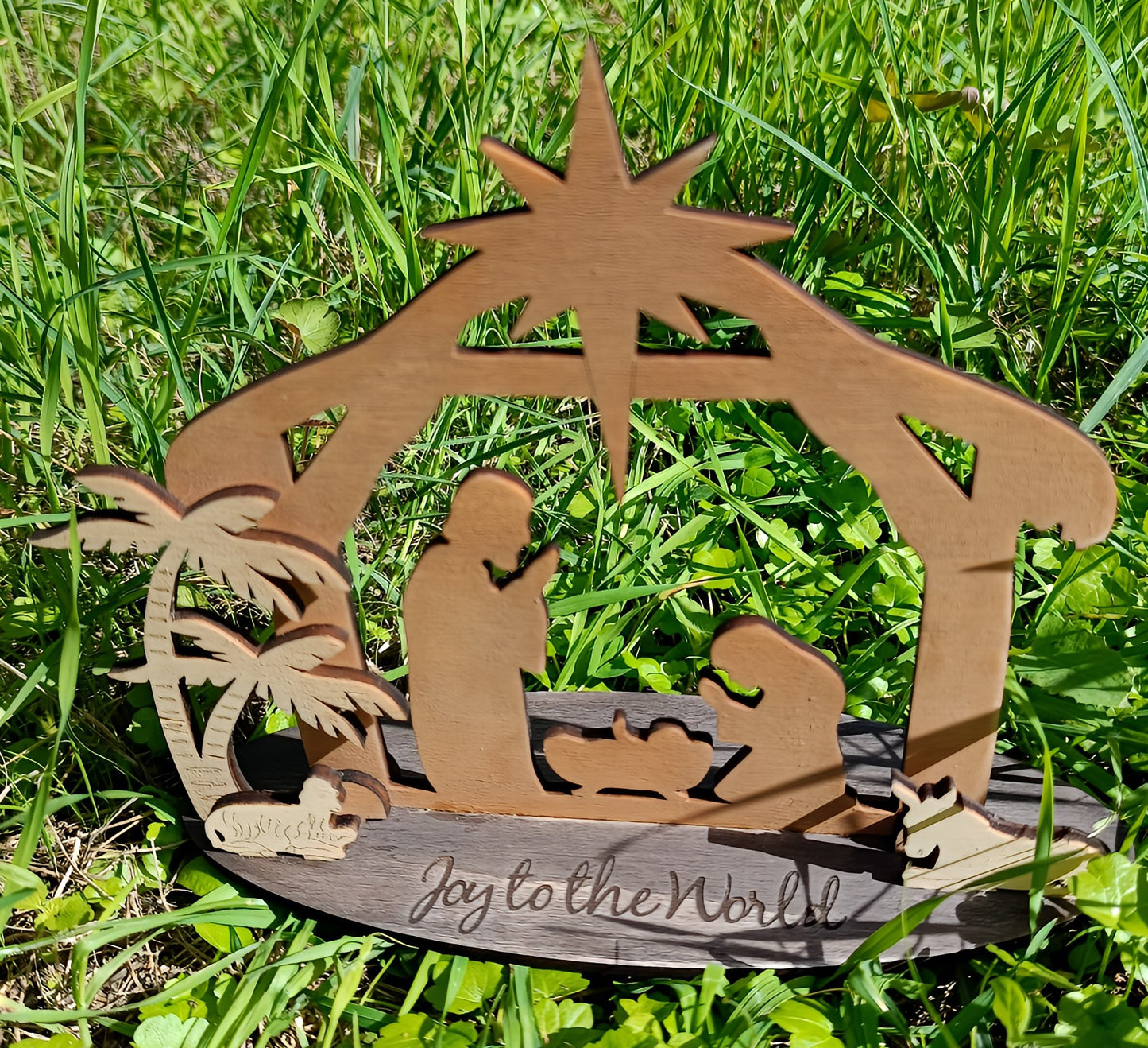 Wooden nativity scene with 'Joy to the World' text on green grass outdoors