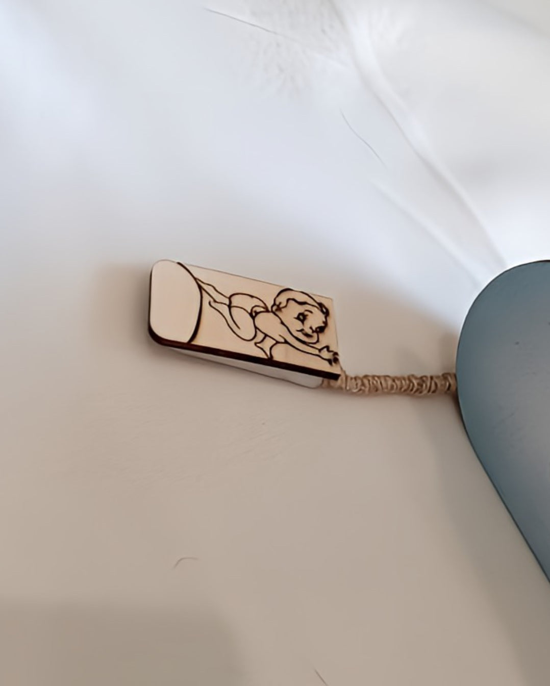 Wooden keychain with engraved cartoon baby on white surface, blue object nearby