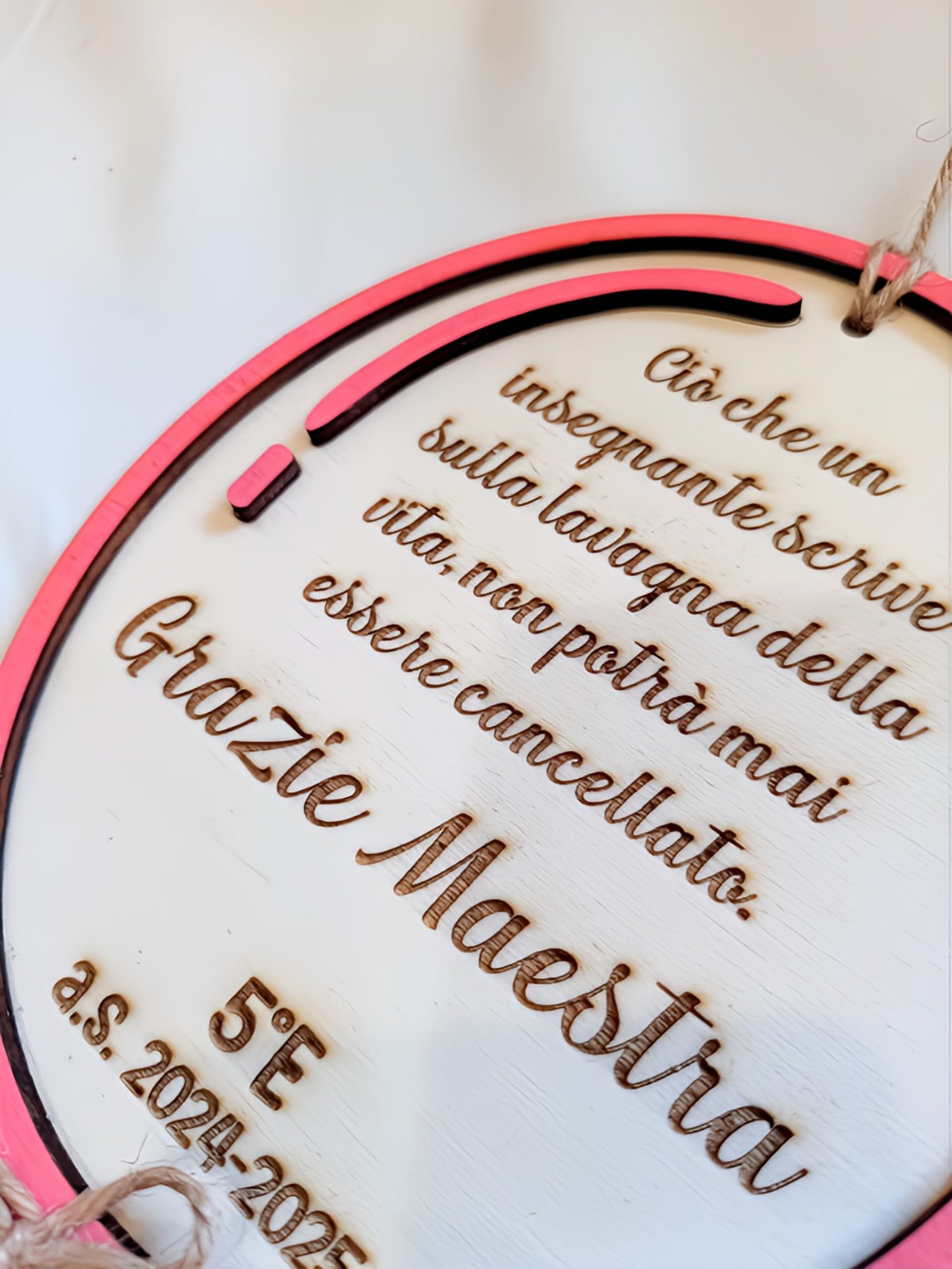 Dettaglio ravvicinato della targa in legno per maestra con cornice in legno multistrato fucsia e strato scuro che crea effetto tridimensionale, matita decorativa rosa sul lato, testo inciso a pirografia in corsivo con frase dedicata all'insegnante. Lavorazione fatto a mano con pirografia su legno dipinto bianco.