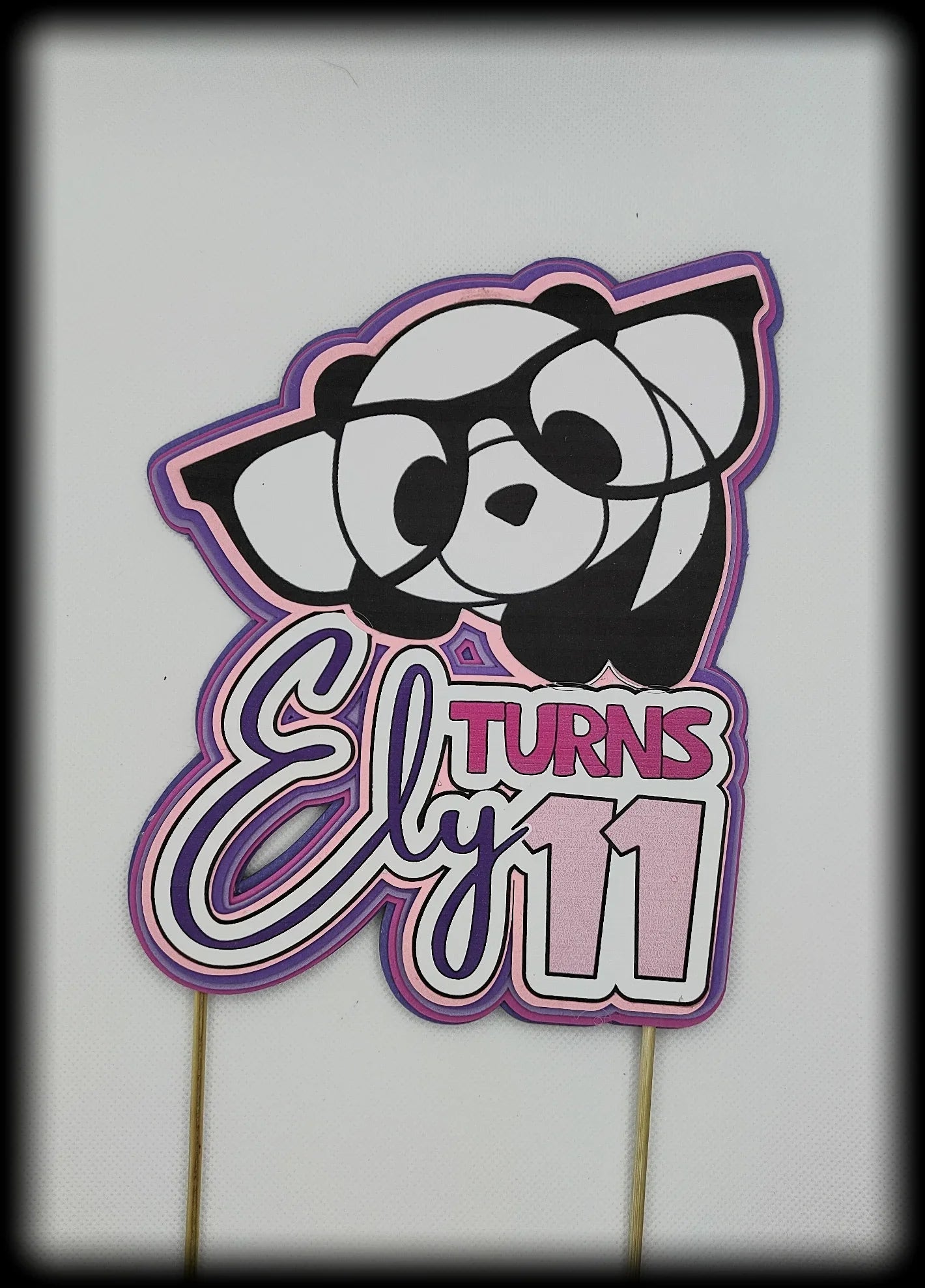 Panda birthday cake topper with glasses, text 'Ely turns 11' in pink and purple.