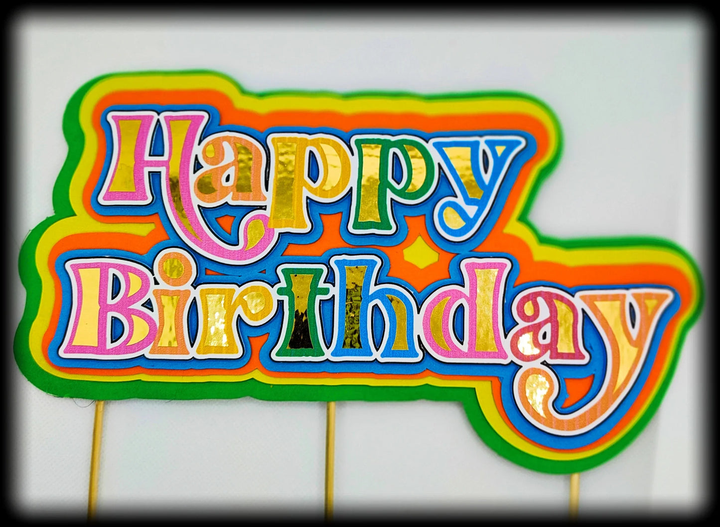 Colorful 'Happy Birthday' sign with bold, layered rainbow letters on a white background.