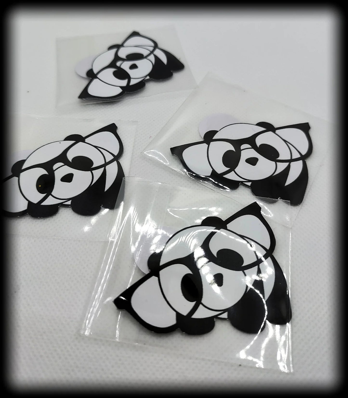 Four black and white panda face stickers on white surface, in clear plastic covers