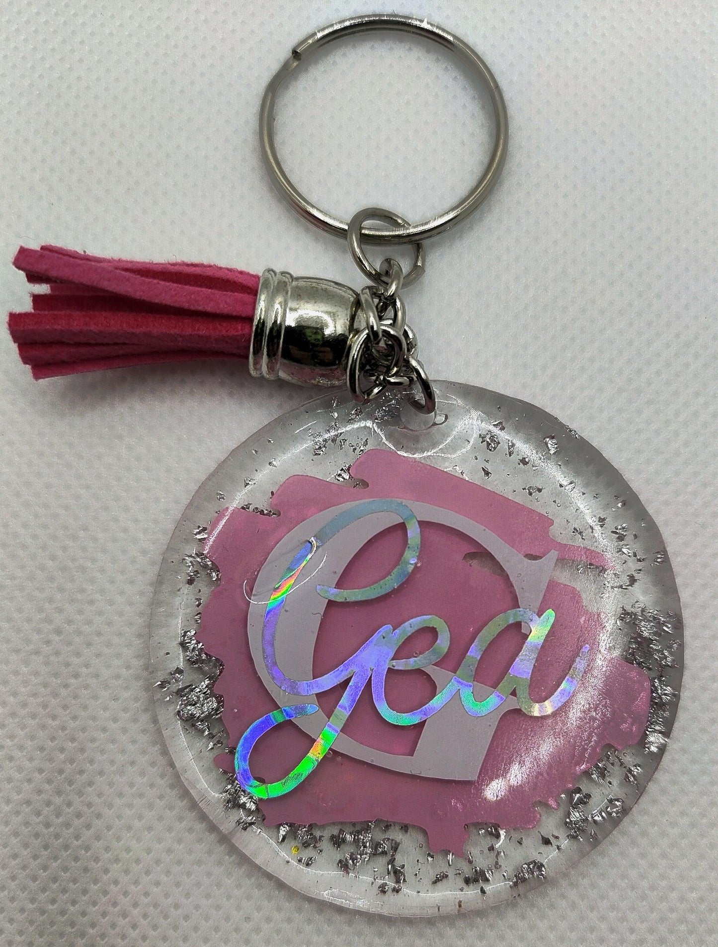Personalized round resin keychain with pink tassel, silver flakes, and holographic 'Gea' text