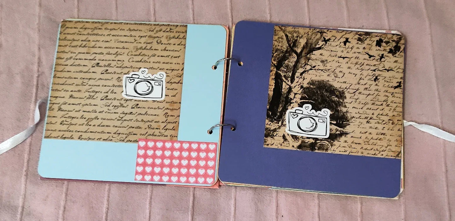 Handmade scrapbook with blue and purple pages, vintage script, heart stickers, and camera icons