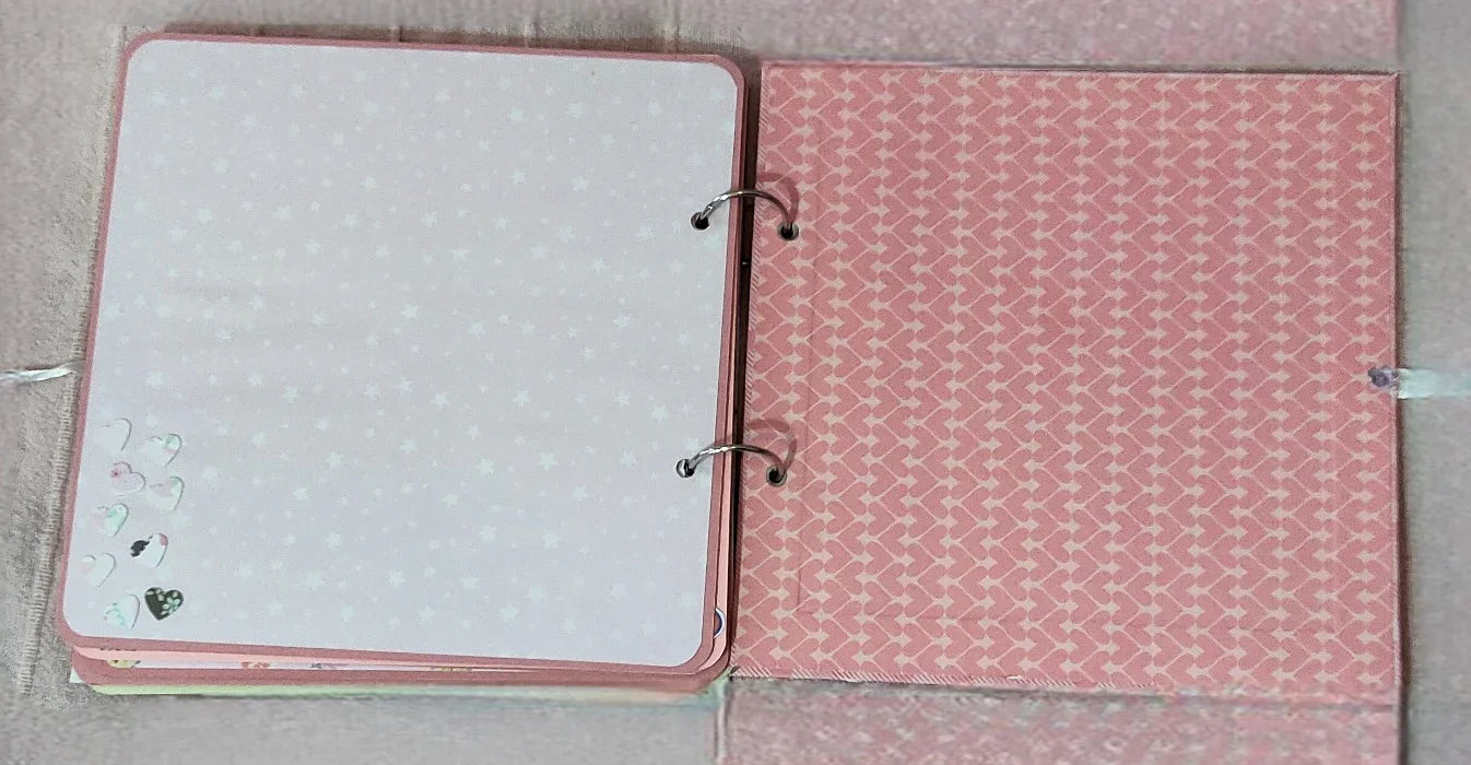 Open pink scrapbook with patterned pages and heart stickers, ideal for memory keeping