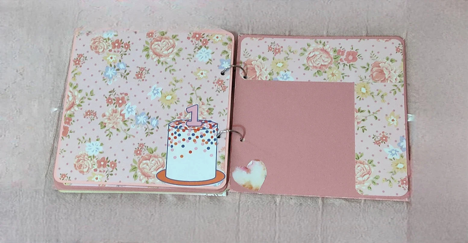 Pink floral scrapbook pages with birthday cake and heart, first birthday photo album.