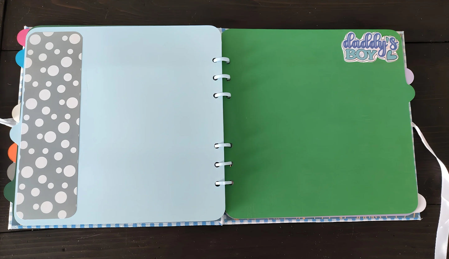 Open scrapbook with blue, green pages and Daddy's Boy sticker, colored tabs visible