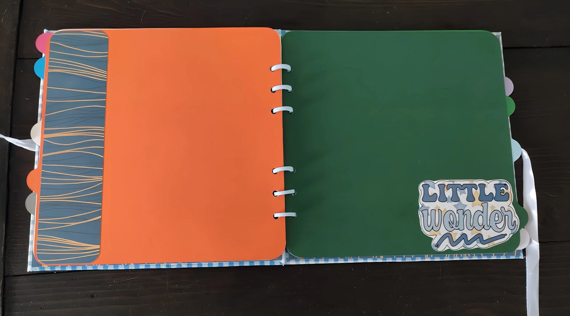 Colorful scrapbook open to orange and green pages, 'Little Wonder' sticker on green page