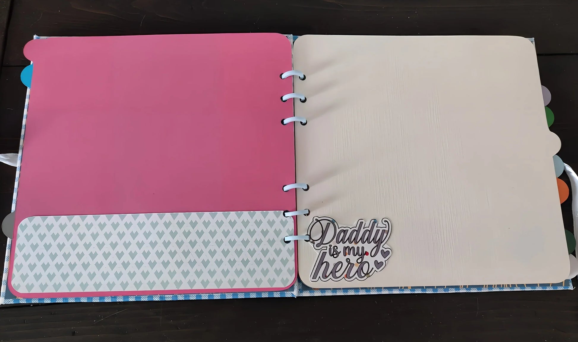Open scrapbook with pink and cream pages, heart pattern, and 'Daddy is my hero' text.