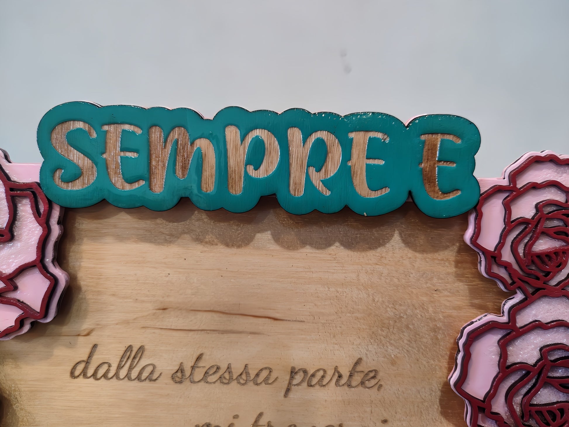 Wooden sign with teal 'SEMPRE E' text and pink floral decorations