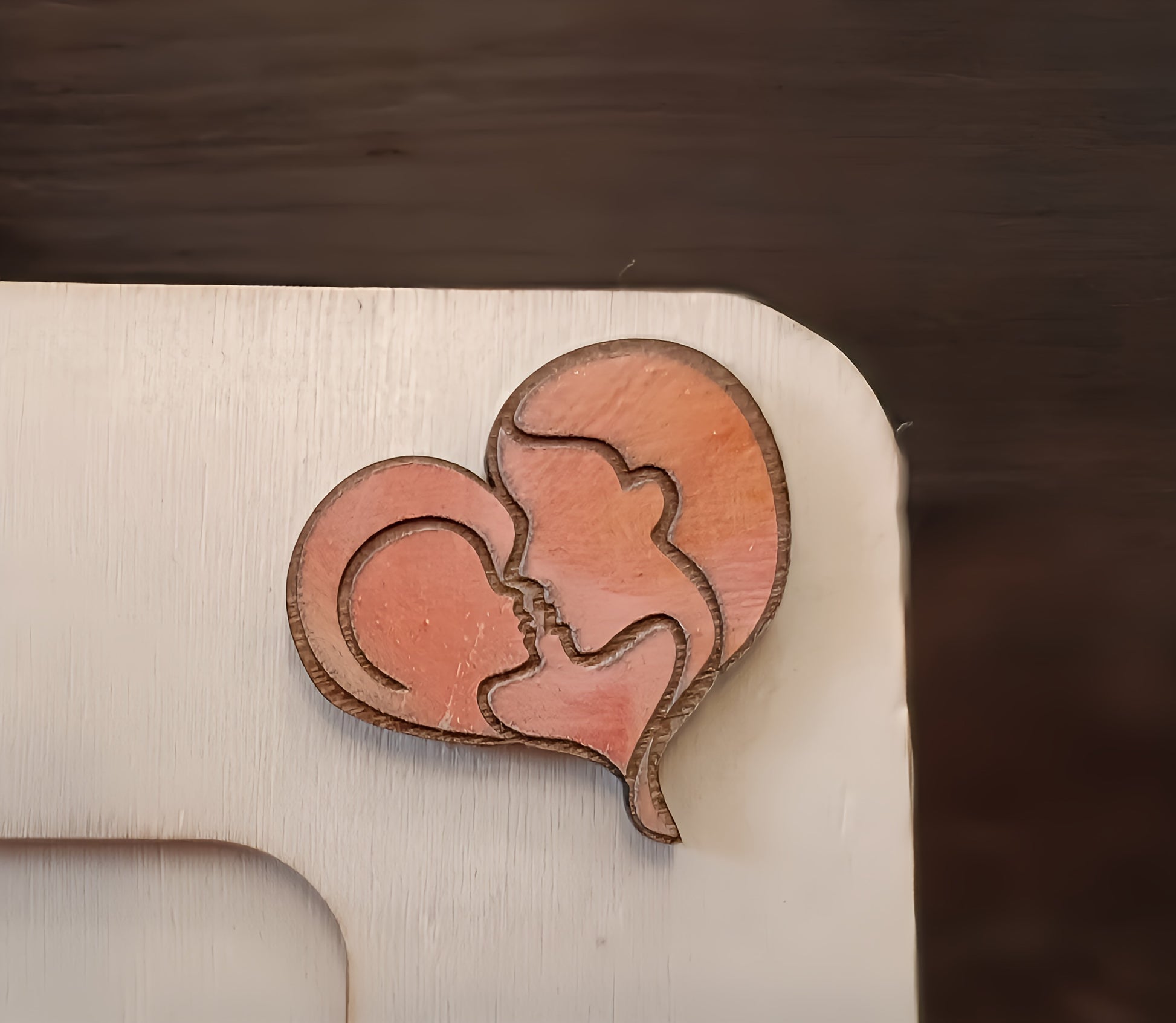 Wooden heart-shaped plaque with engraved profiles of a mother and child on a white surface