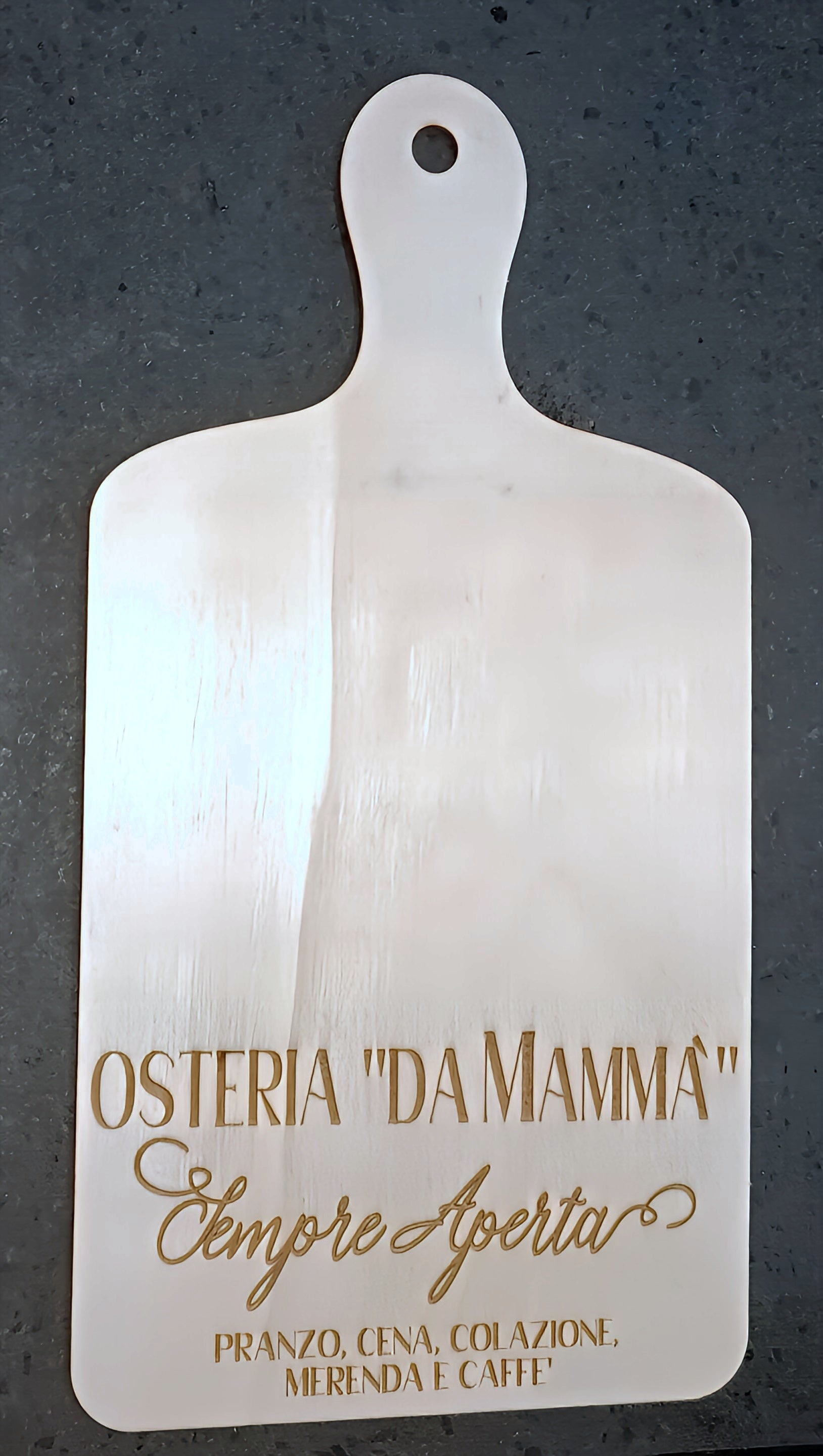 Wooden cutting board with 'Osteria Da Mammà' engraved, on a dark stone surface