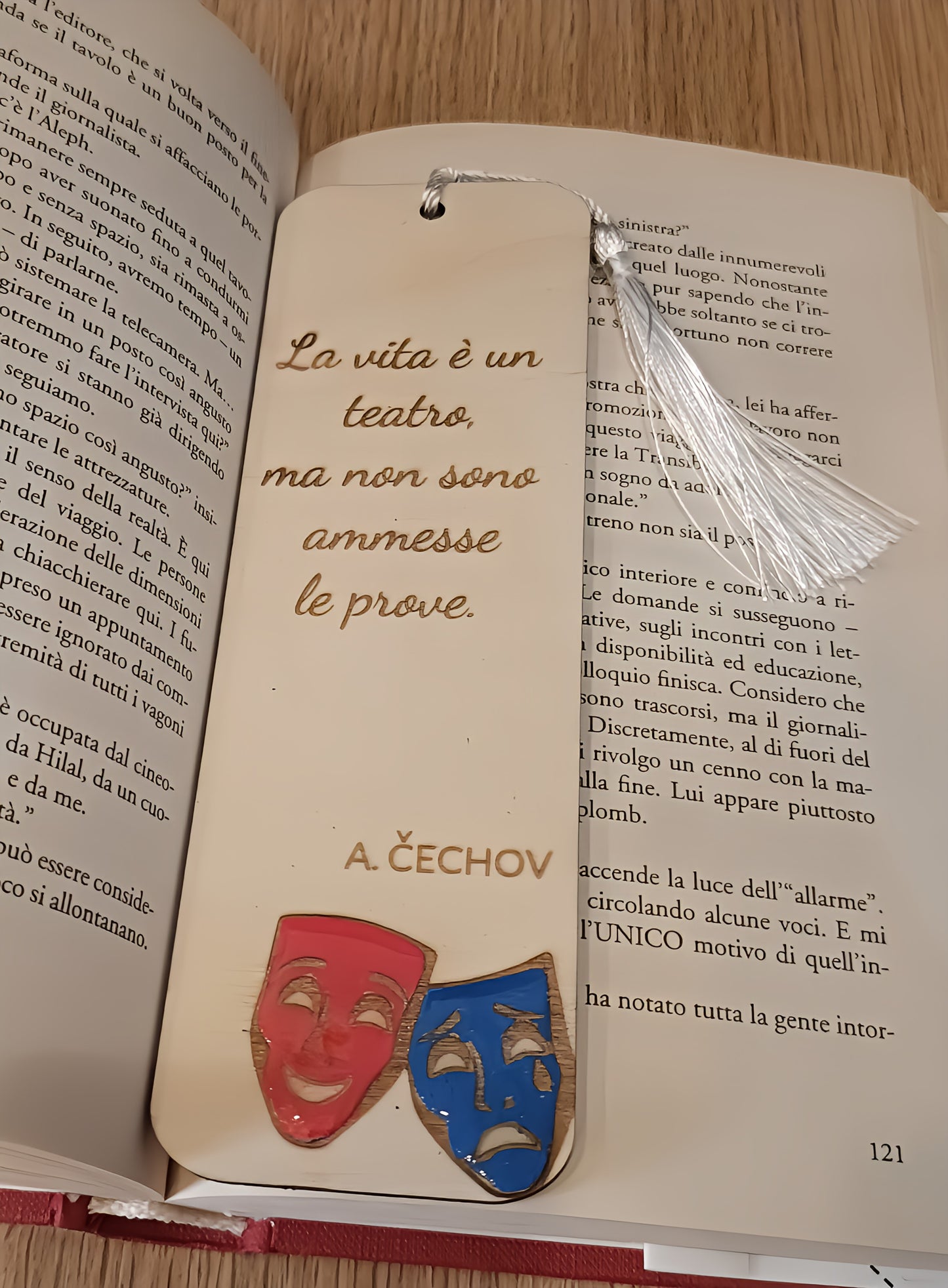 Wooden bookmark with Italian quote and theater masks on an open book on wooden table