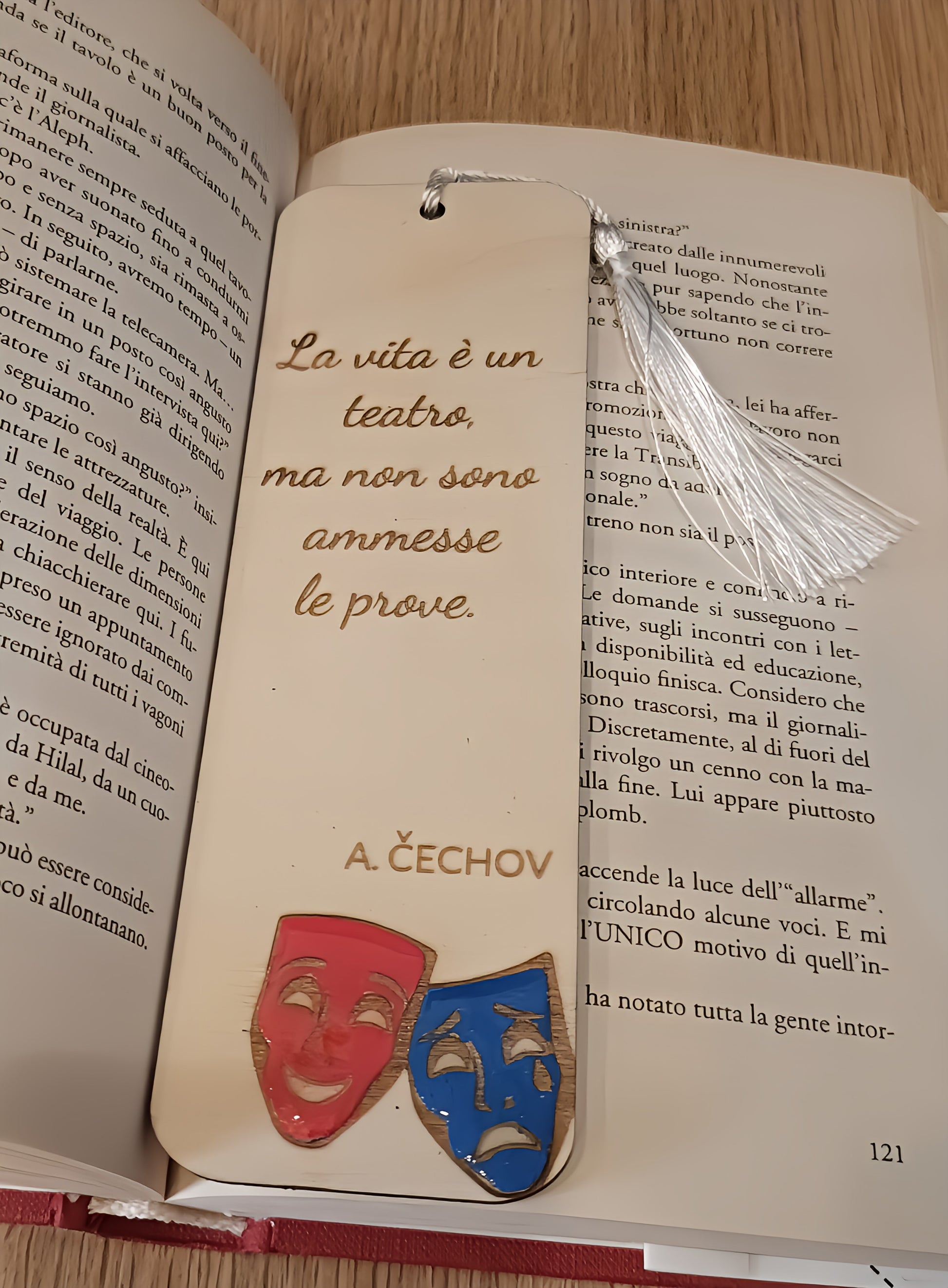 Wooden bookmark with Italian quote and theater masks on an open book on wooden table