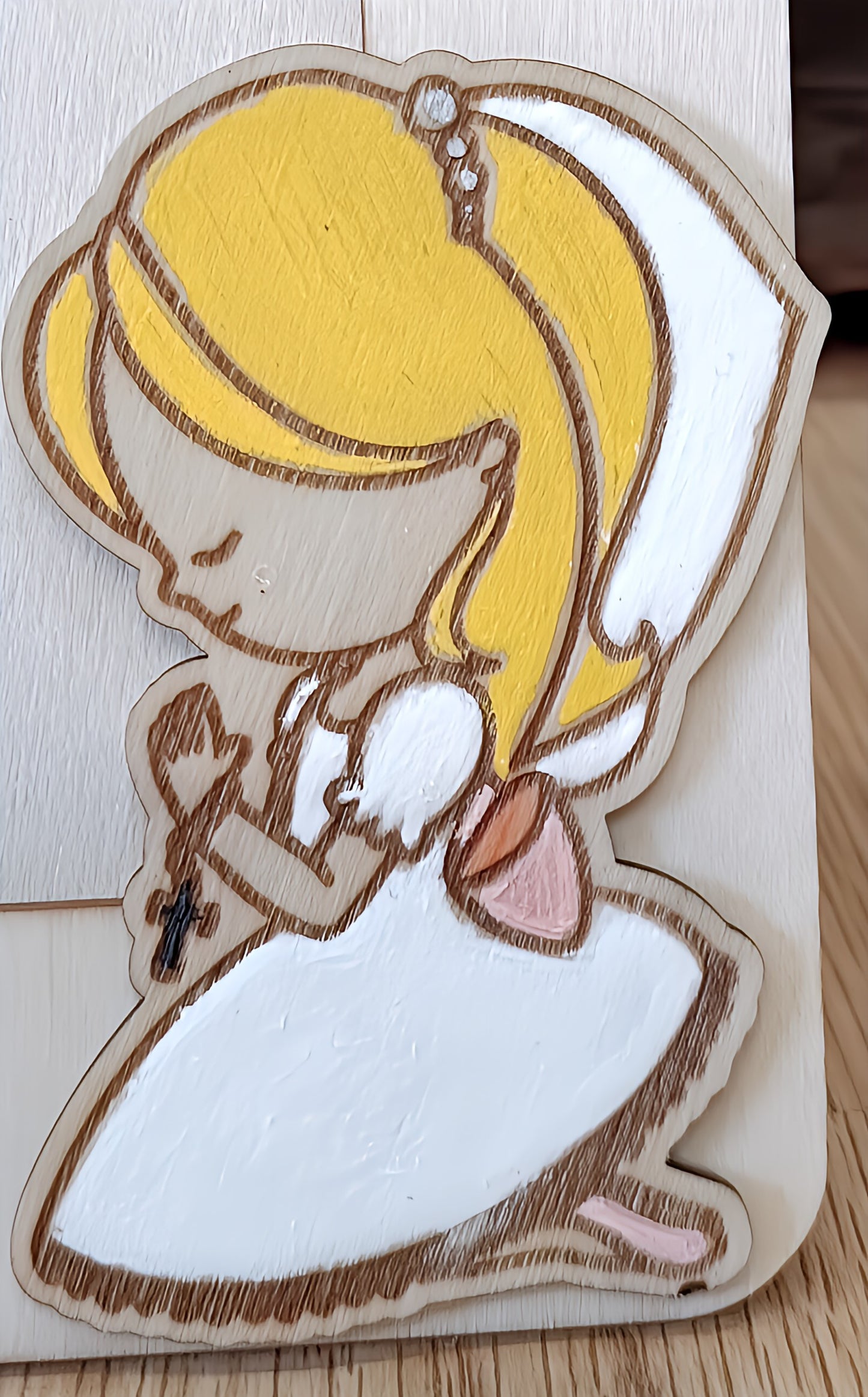 Wooden cutout of blonde girl angel in white dress kneeling and praying with a cross