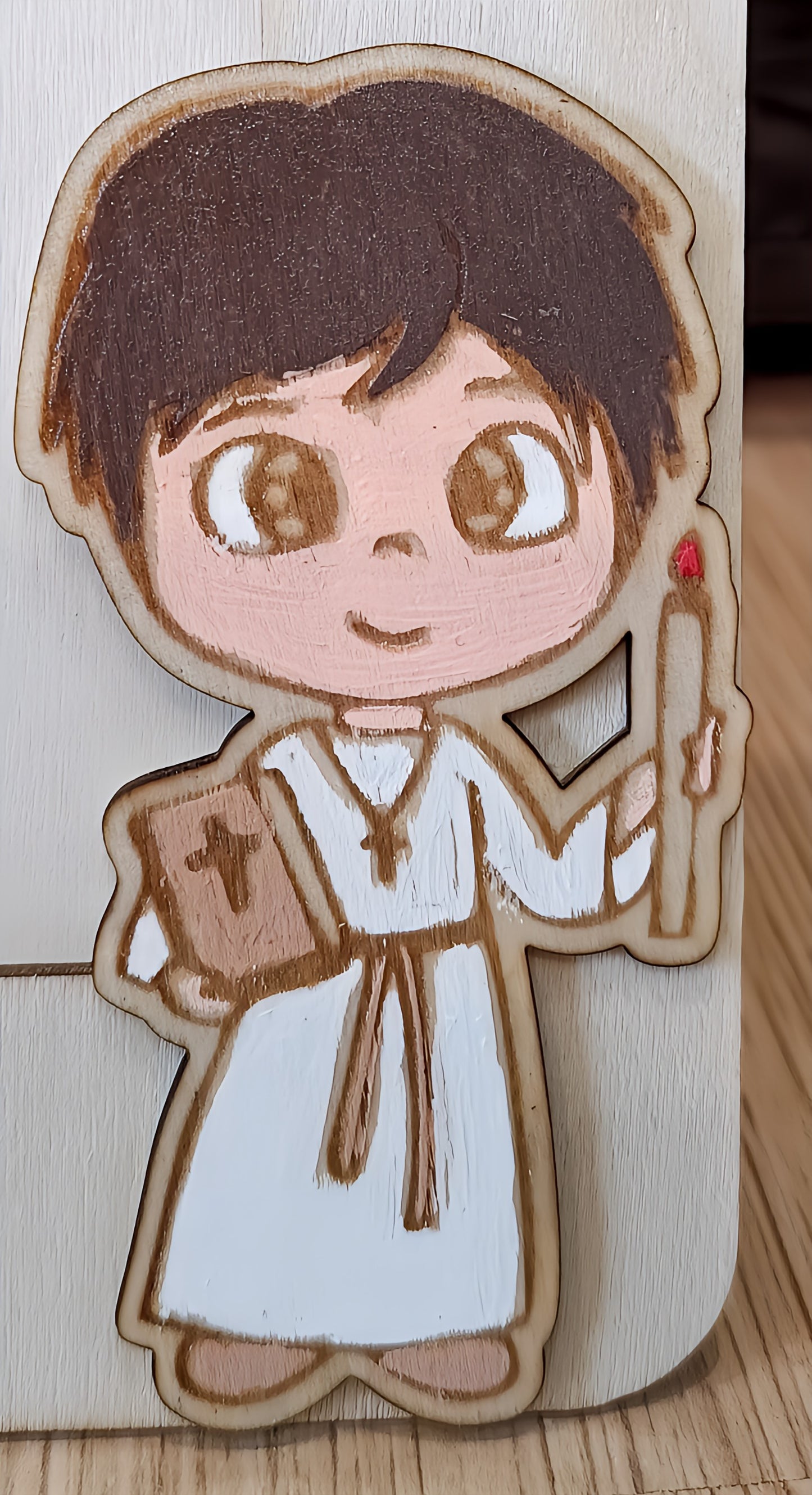Wooden figure of a child acolyte holding a Bible and candle on light wood background
