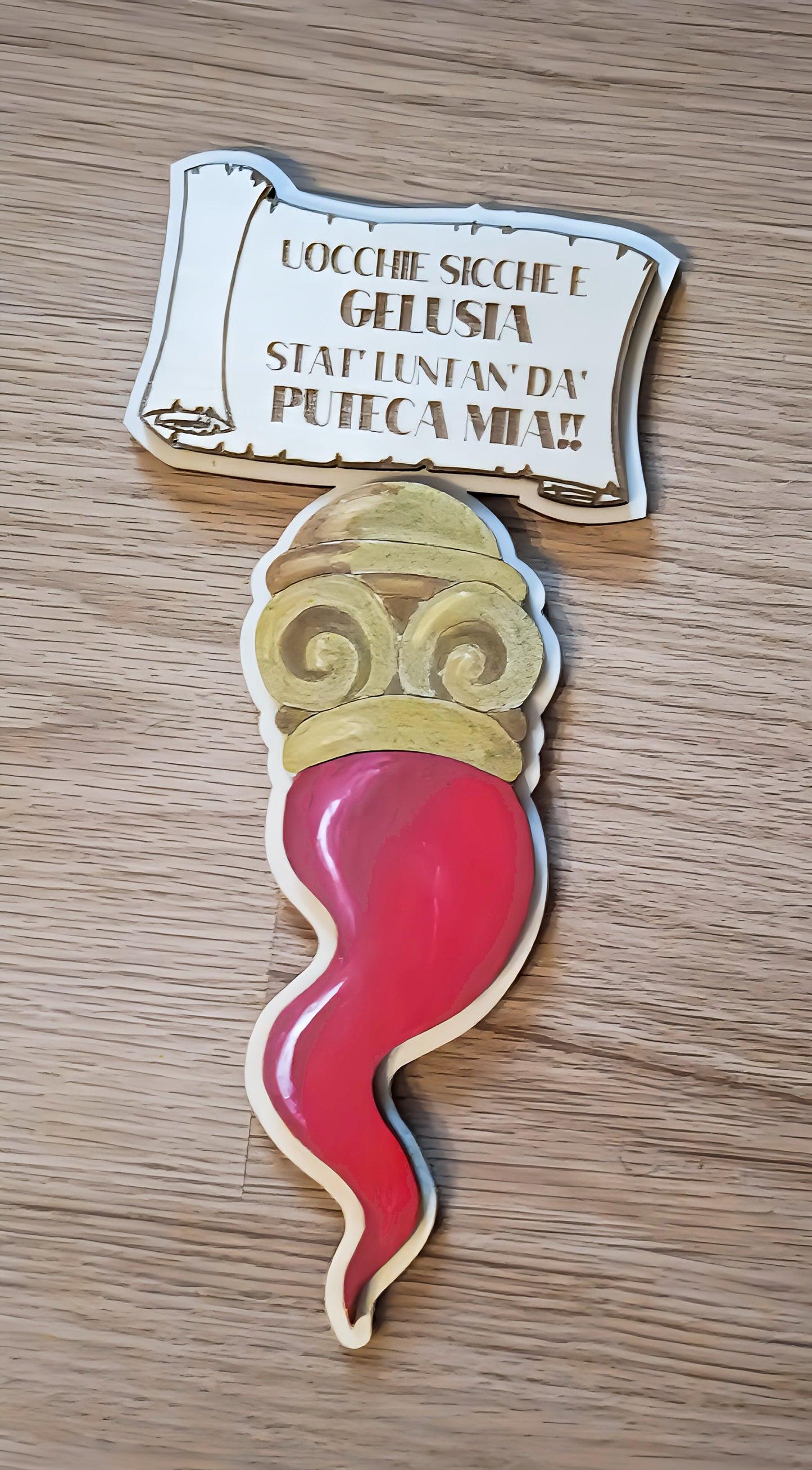 Wooden Italian cornicello charm with engraved message on light wood surface