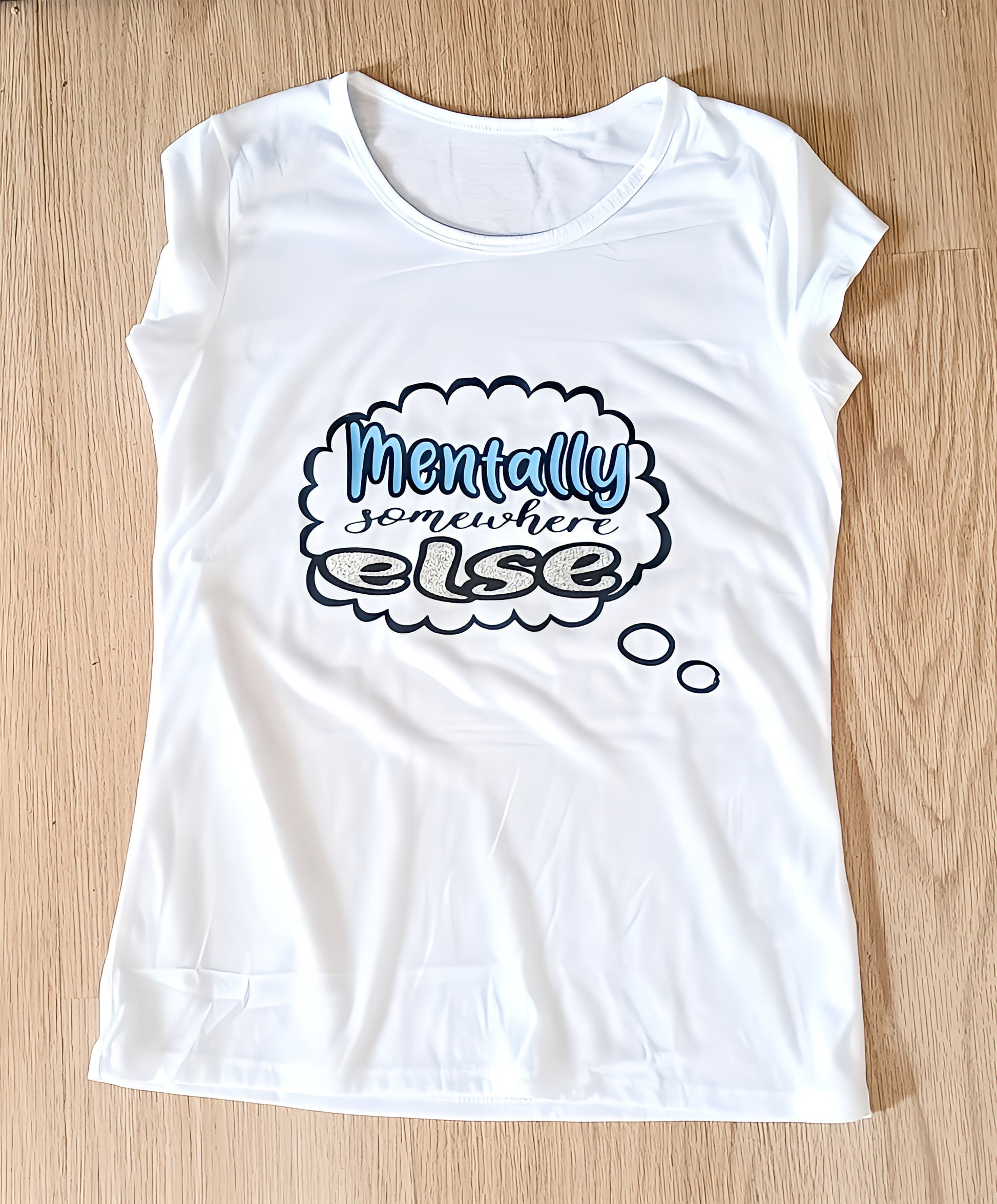 White t-shirt with 'Mentally somewhere else' text design on wooden floor
