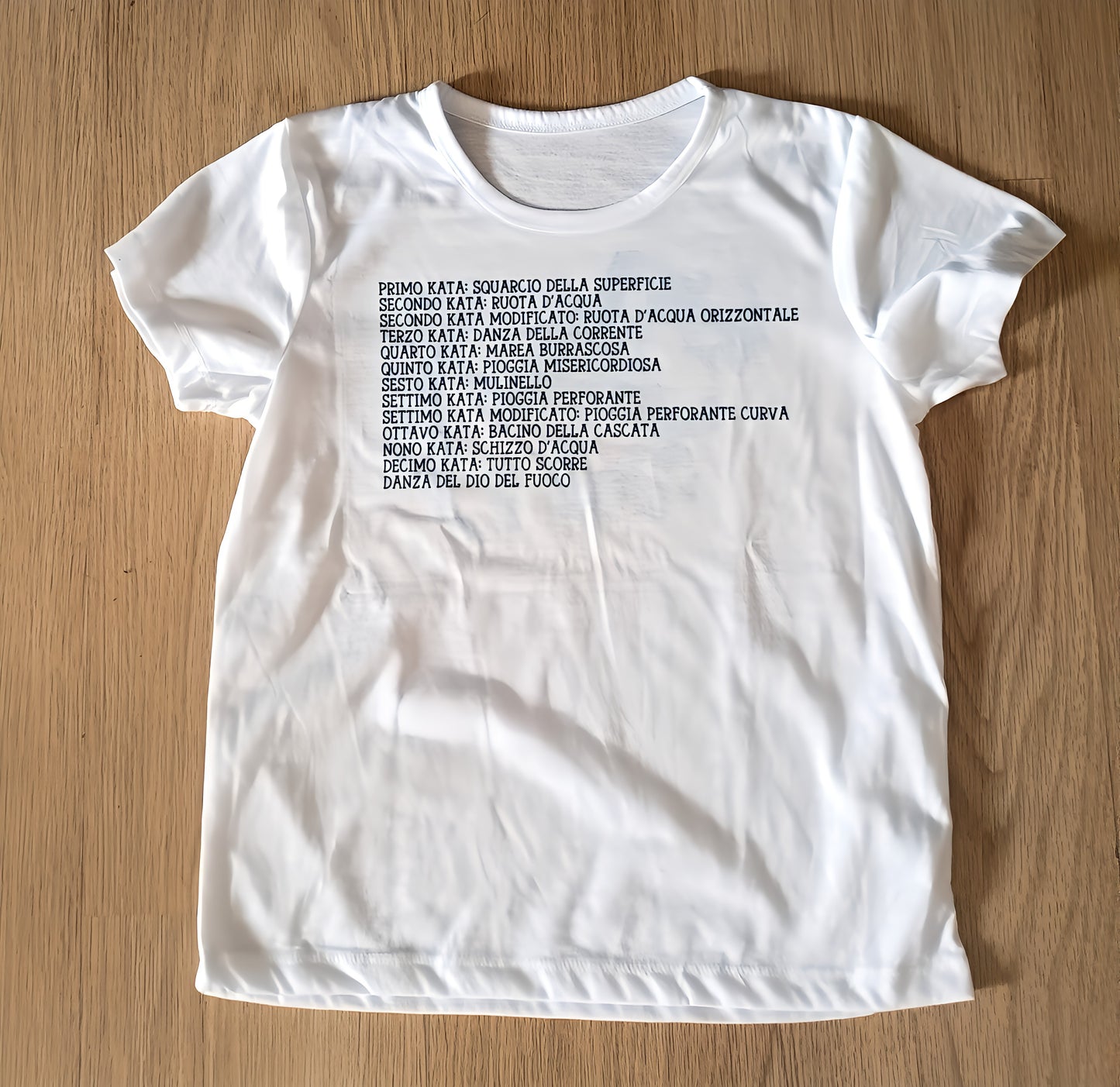 White t-shirt on wood surface with Italian kata list text printed in black