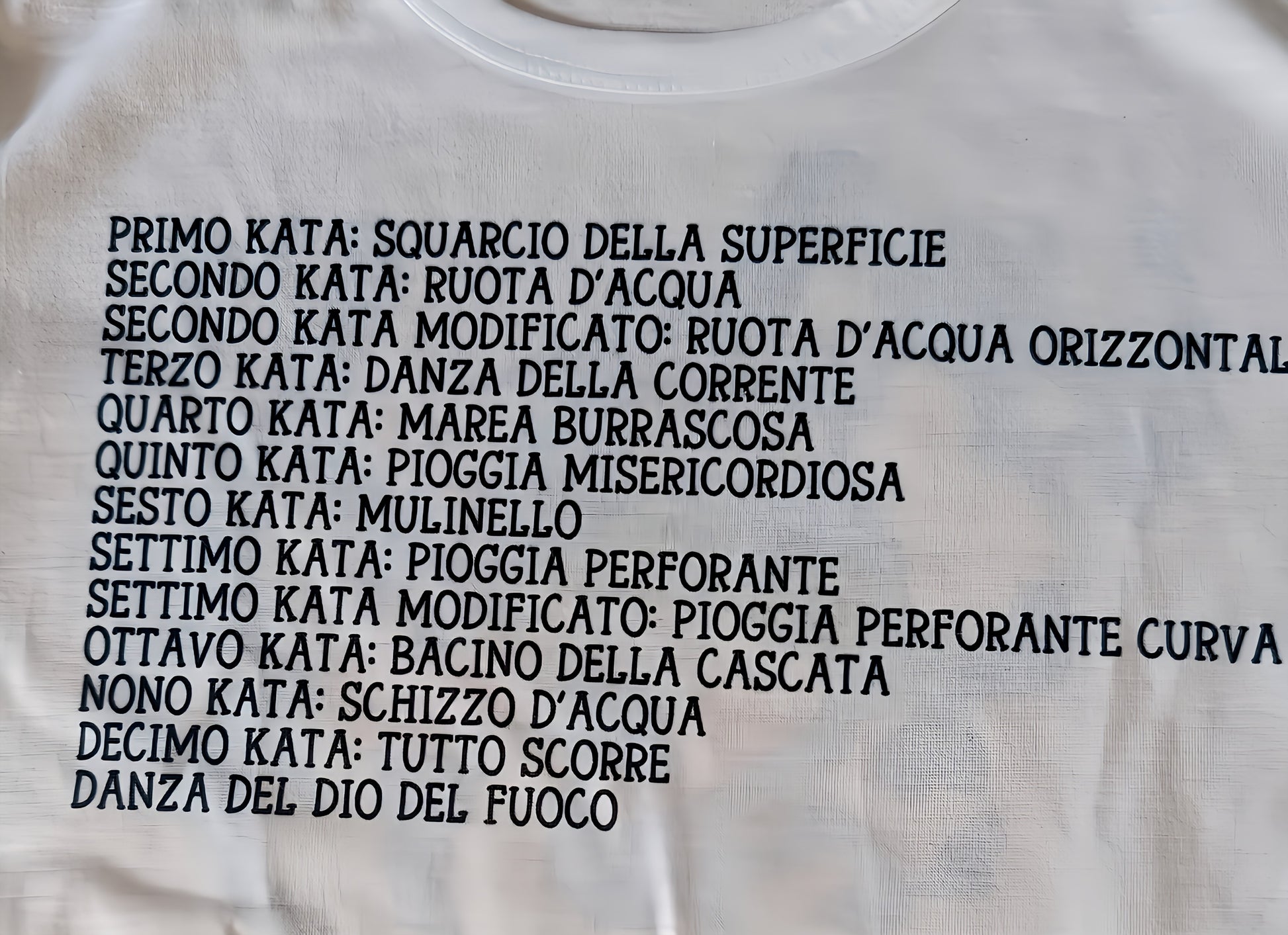 White t-shirt with Italian text listing kata moves in bold black letters