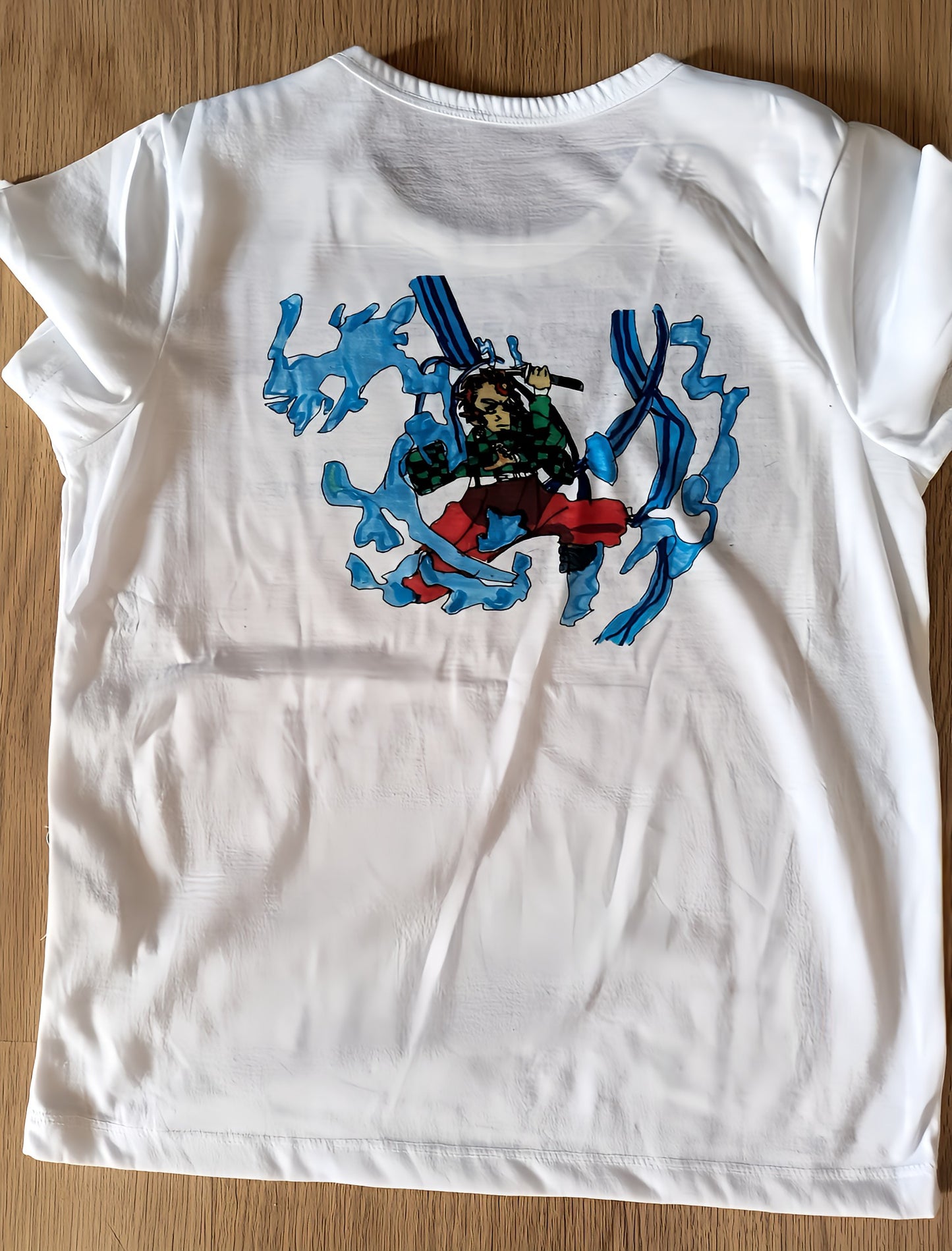 White t-shirt with anime-style warrior and blue wave graphic on the back, laid on wood