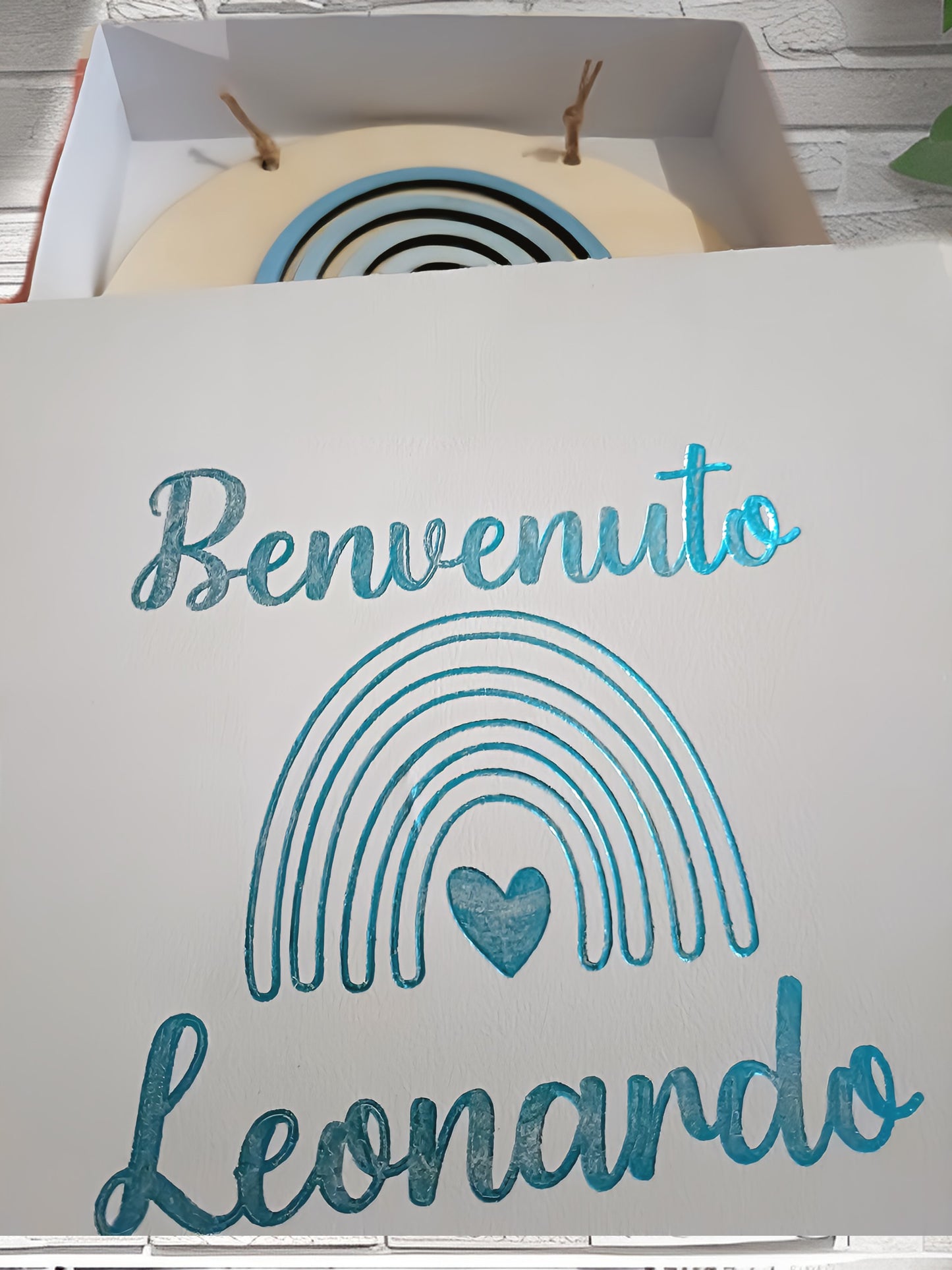 White gift box with 'Benvenuto Leonardo' in blue, rainbow and heart design, wall background
