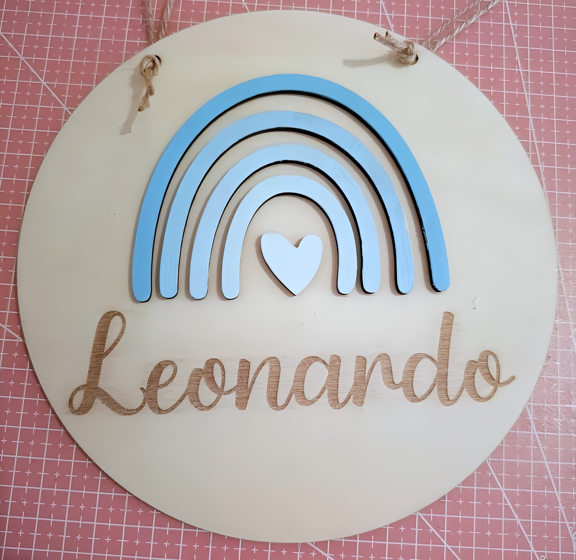 Round wooden nursery name sign with blue rainbow, heart, and Leonardo text on pink background