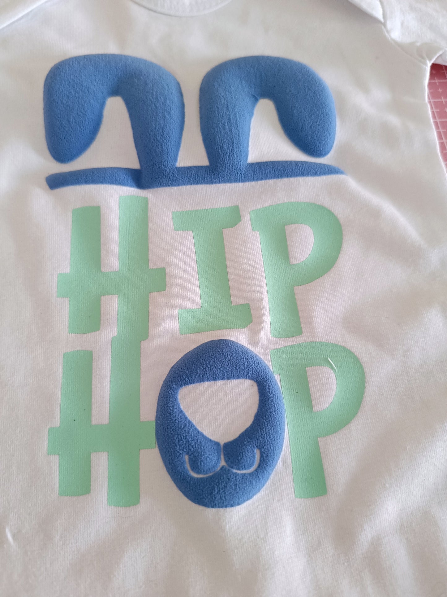 White baby onesie with blue bunny ears, snout and green hashtag HIP HOP text design