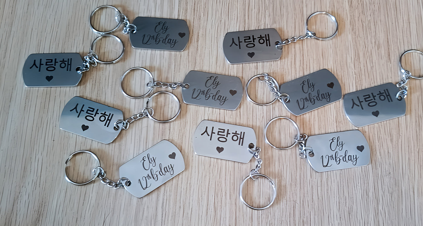 Metal keychains on wood table engraved with 'Ely 12th b-day' and '사랑해' with heart