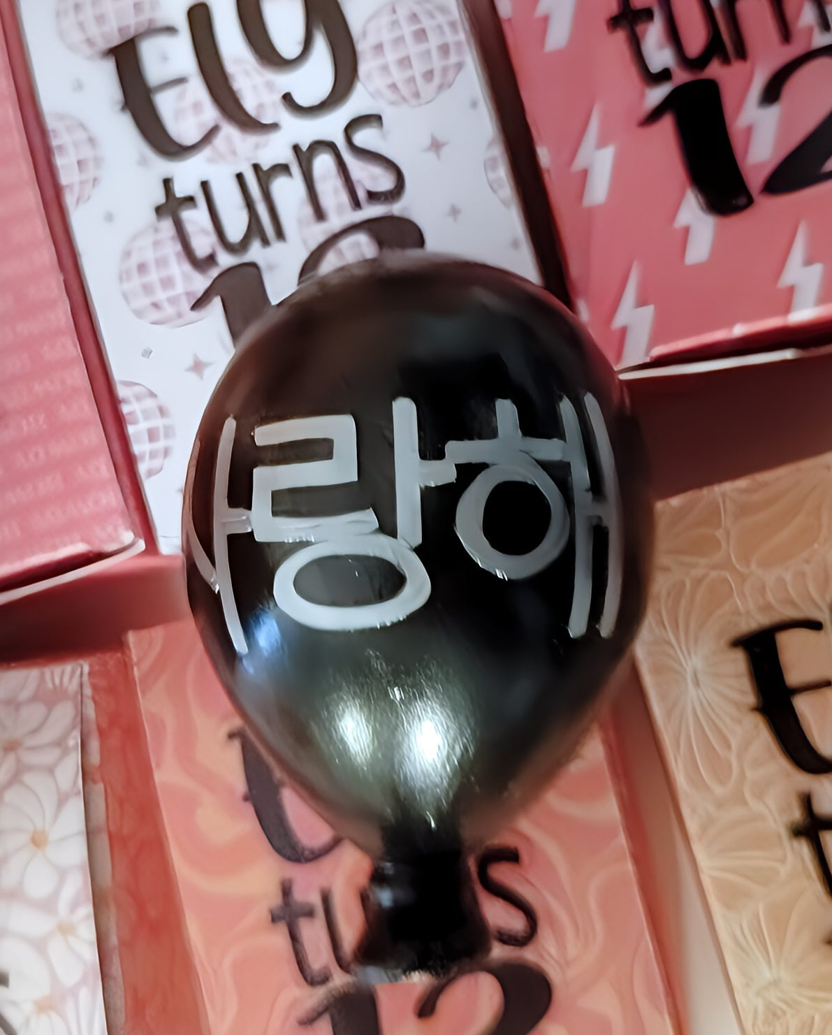 Black balloon with Korean text, surrounded by pink birthday cards reading 'Ely turns 12'.