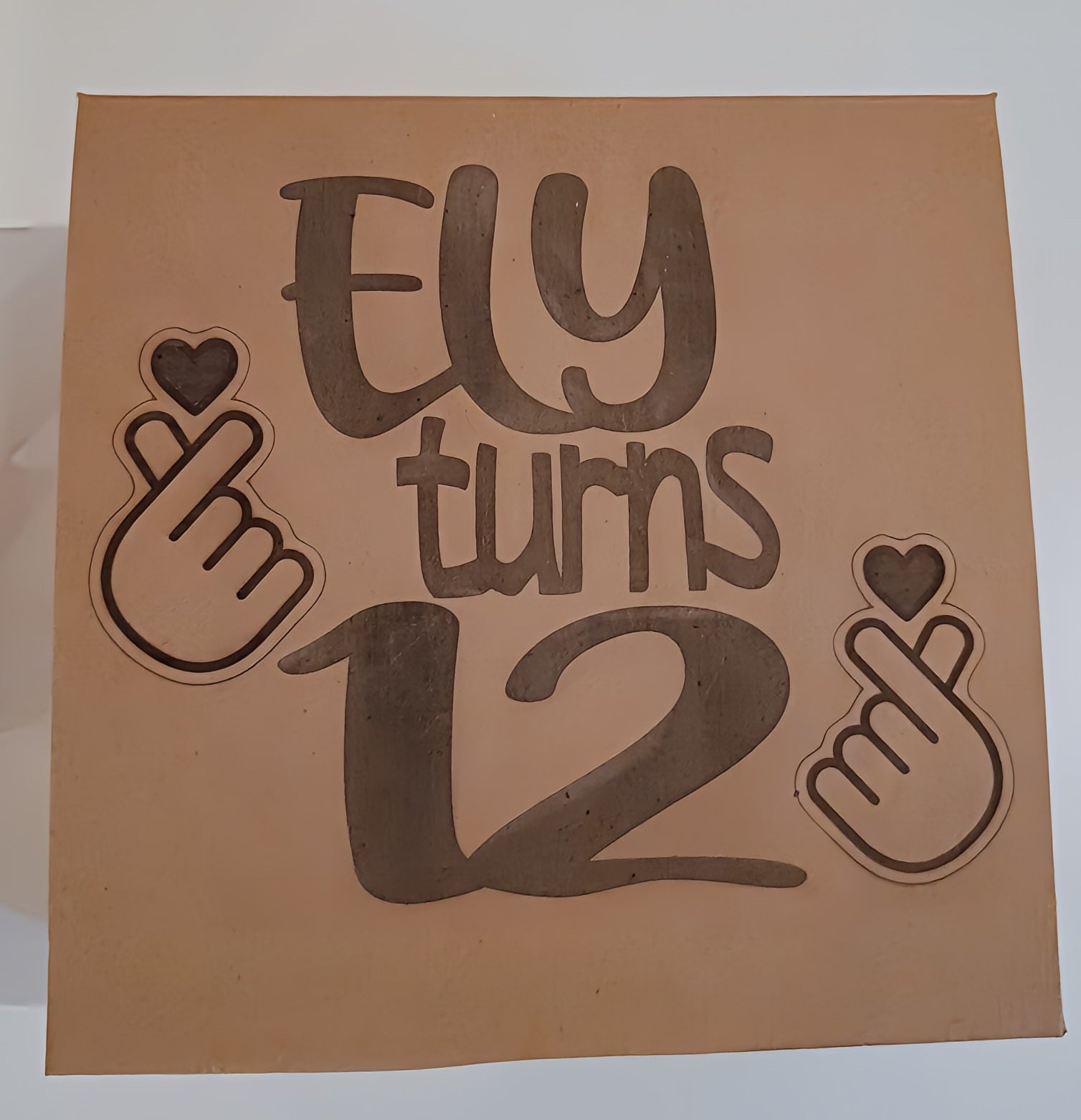 Brown gift box with 'Ely turns 12' and hand heart signs for birthday celebration