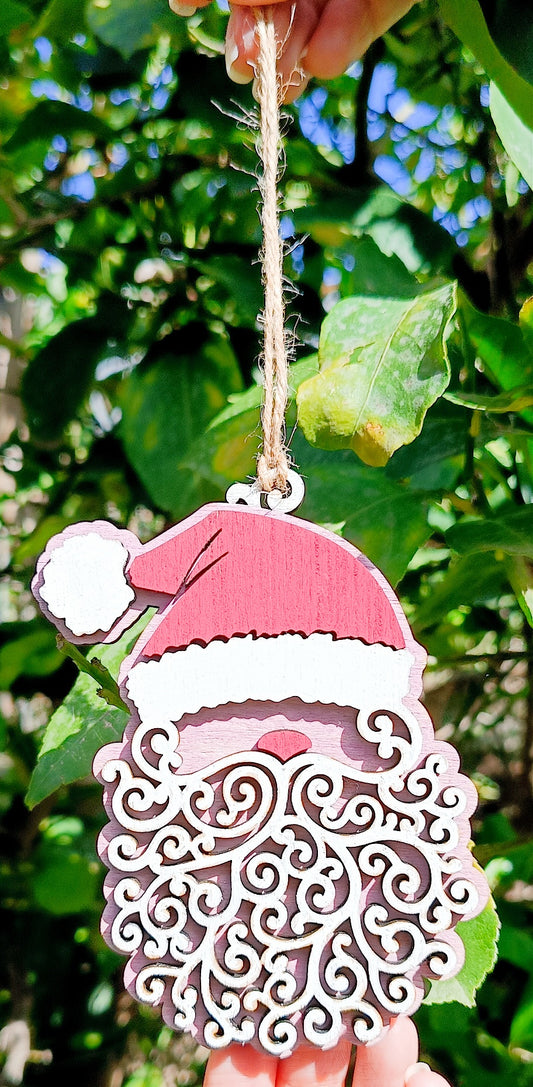 Wooden Santa Claus Christmas ornament with curly beard held outdoors by string, green leaves background