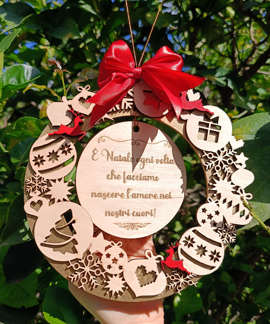 Hand holding wooden Christmas wreath ornament with red bow and Italian holiday message, outdoors