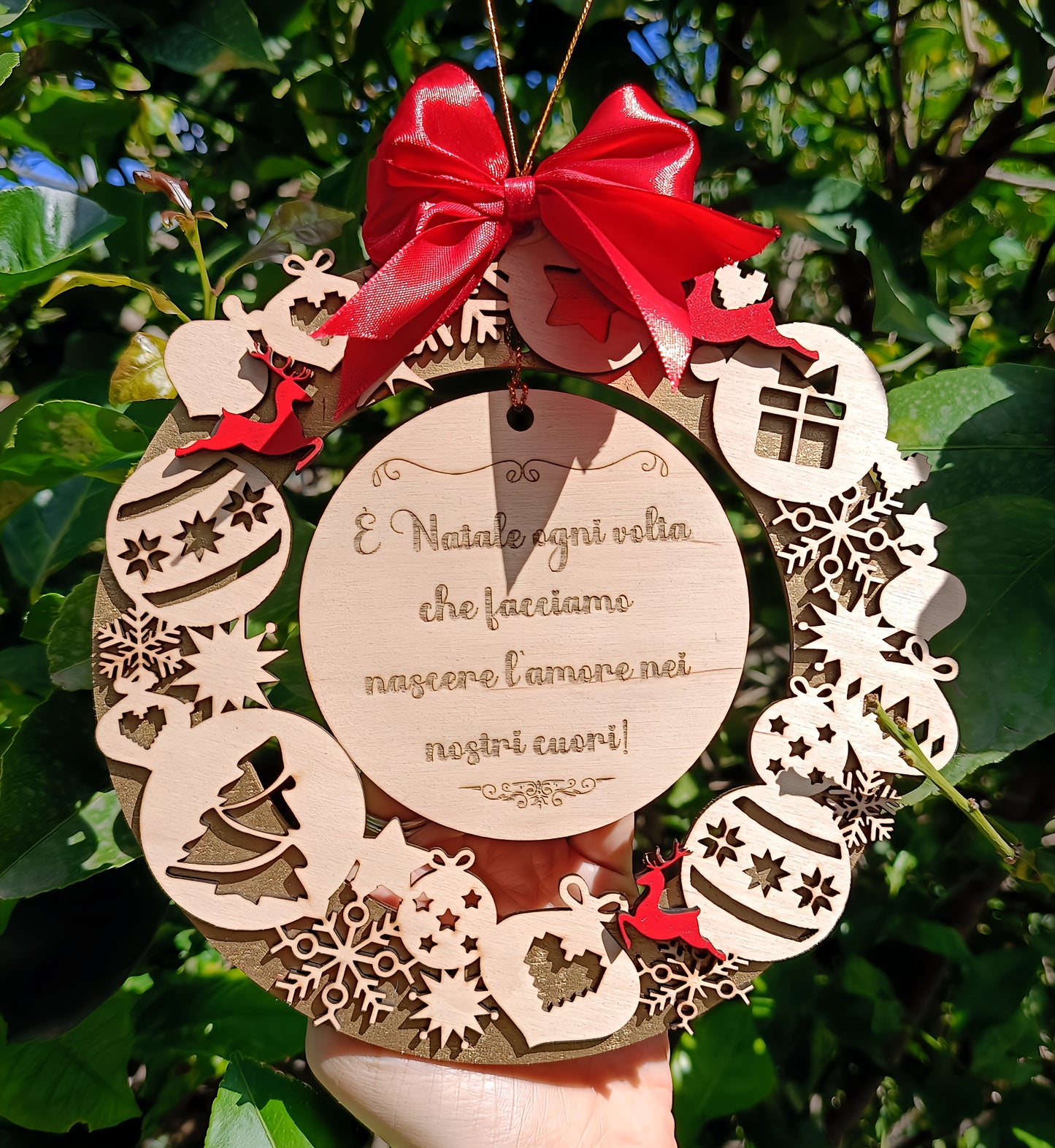 Engraved wooden Christmas wreath with red bow, ornaments and Italian text, held outdoors