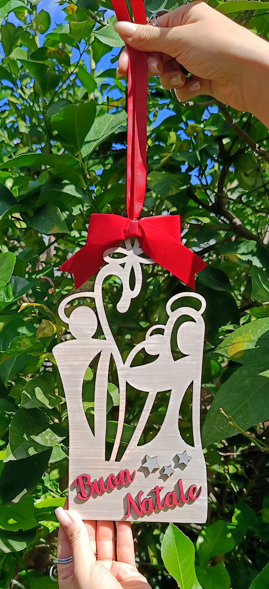 Wooden nativity Christmas ornament with red bow and Buon Natale text, held outdoors among green leaves