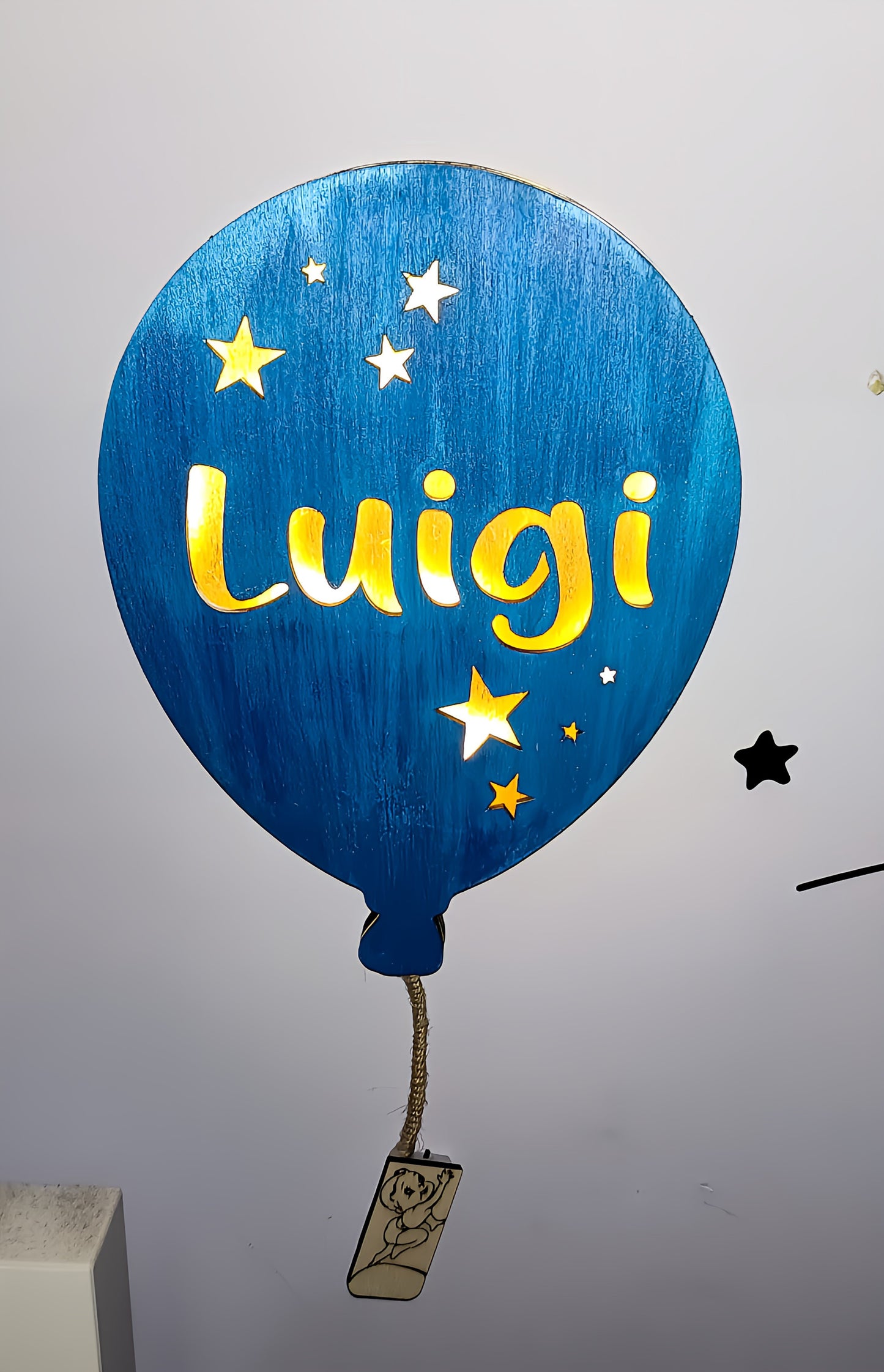 Blue balloon-shaped night light with stars and the name Luigi on a white wall