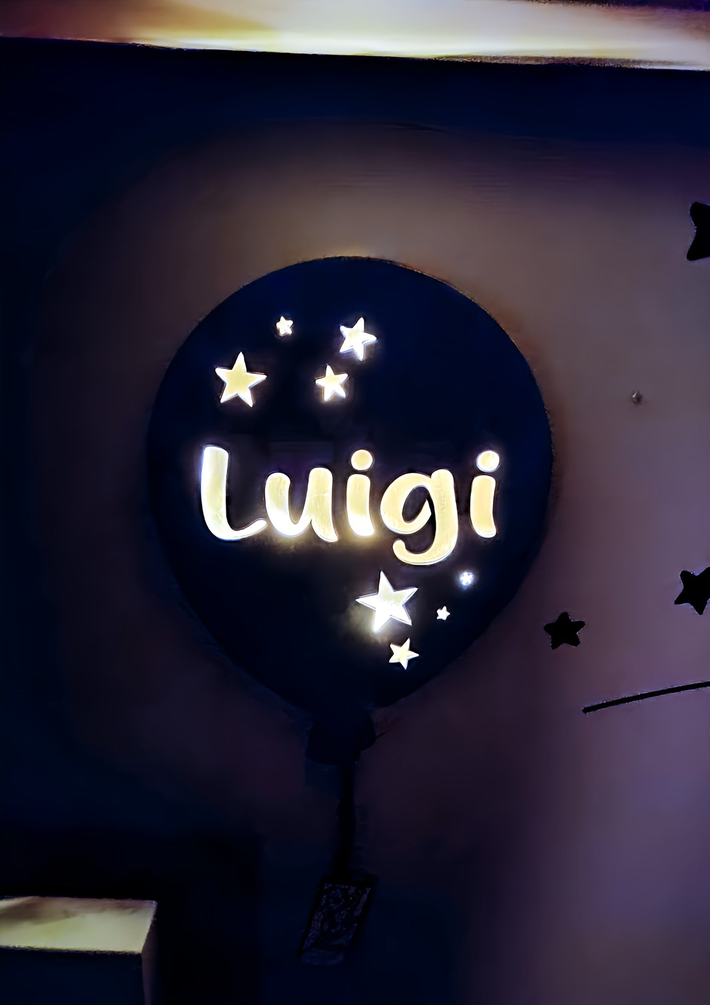 Glowing wall-mounted night light shaped like a balloon with stars and 'Luigi' text, dark room