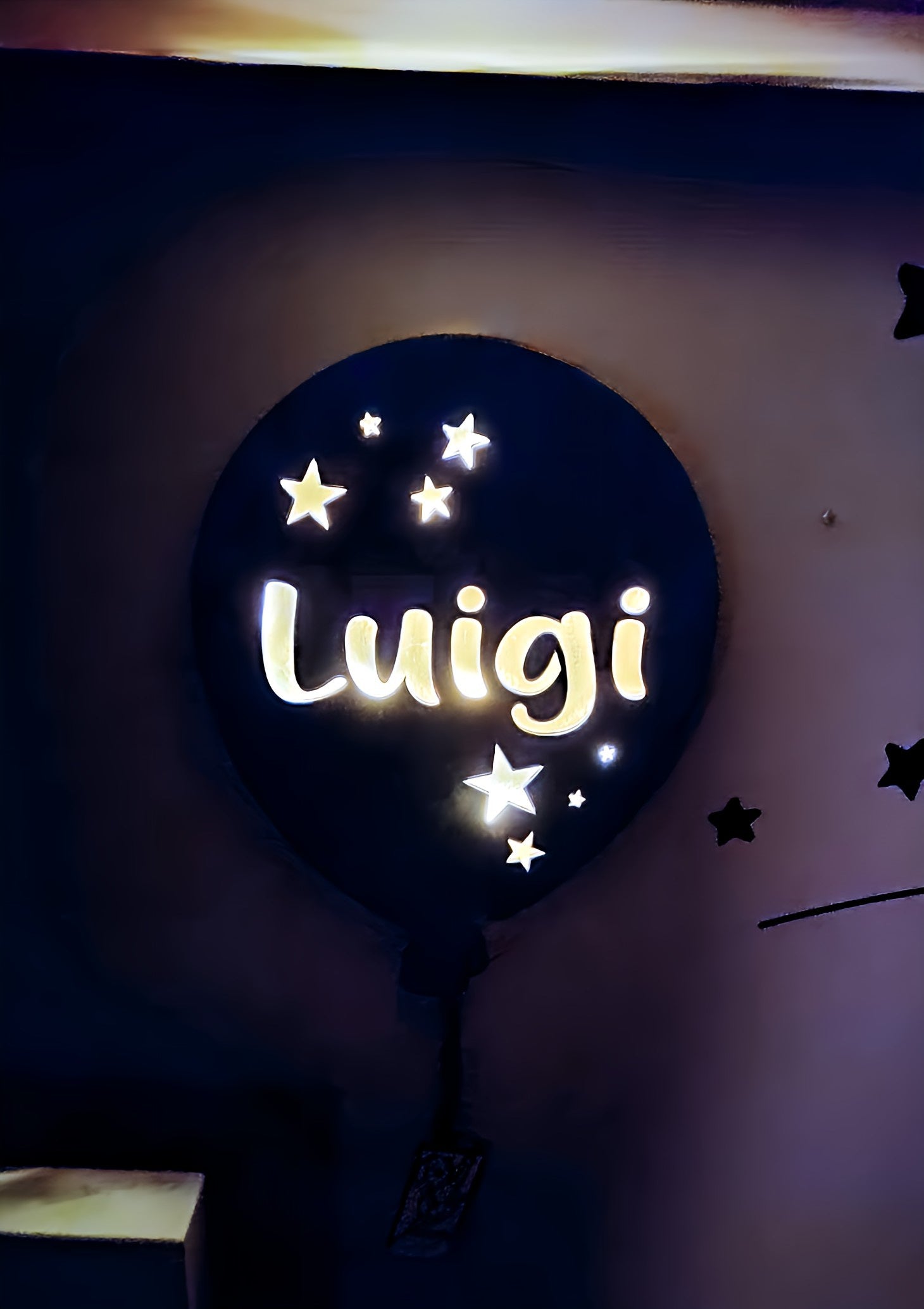 Glowing wall-mounted night light shaped like a balloon with stars and 'Luigi' text, dark room