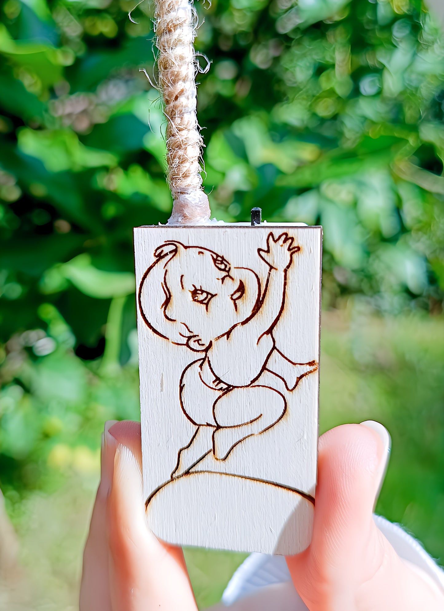 Wooden tag with engraved baby design held outdoors, handmade jewelry accessory