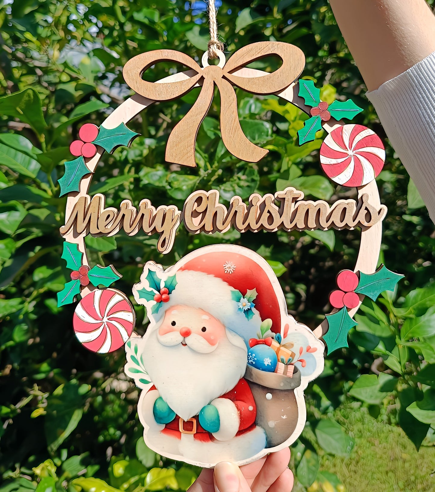 Wooden Merry Christmas Santa wreath ornament with holly and candy, held outdoors