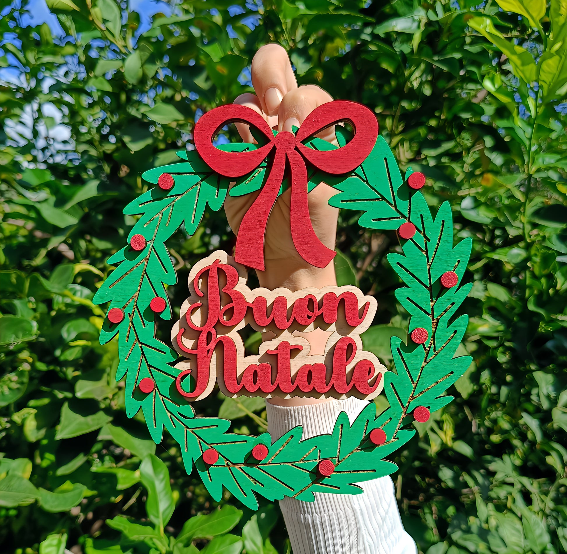 Hand holding green Christmas wreath with red bow and Buon Natale sign outdoors