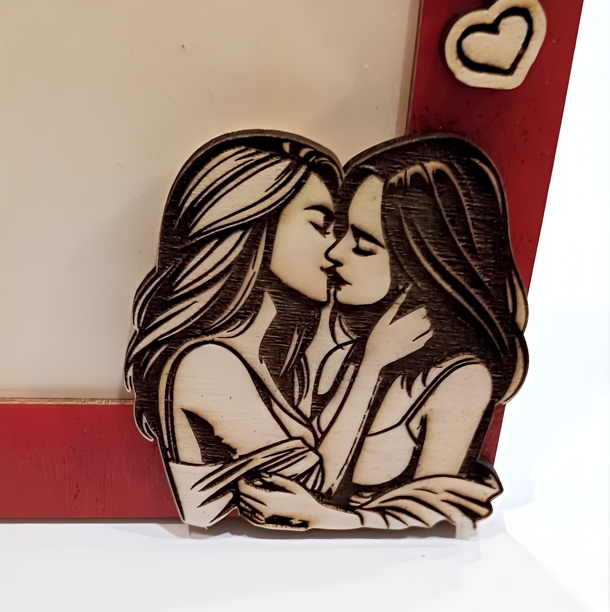 Wooden engraving of two women kissing on a red photo frame with heart detail