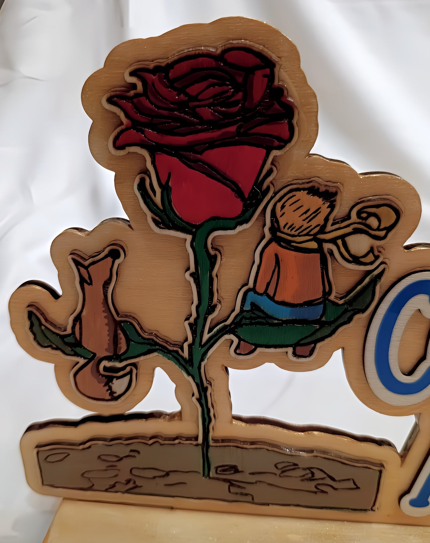 Wooden engraved art of a red rose, fox, and child with scarf on green leaf, white background