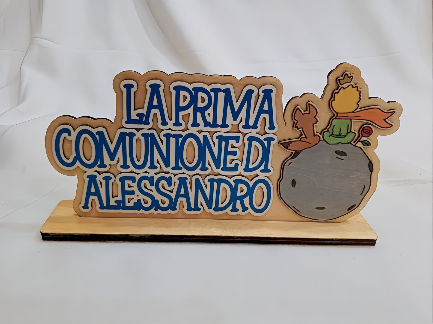 Wooden plaque with blue text 'La Prima Comunione di Alessandro' and Little Prince figure
