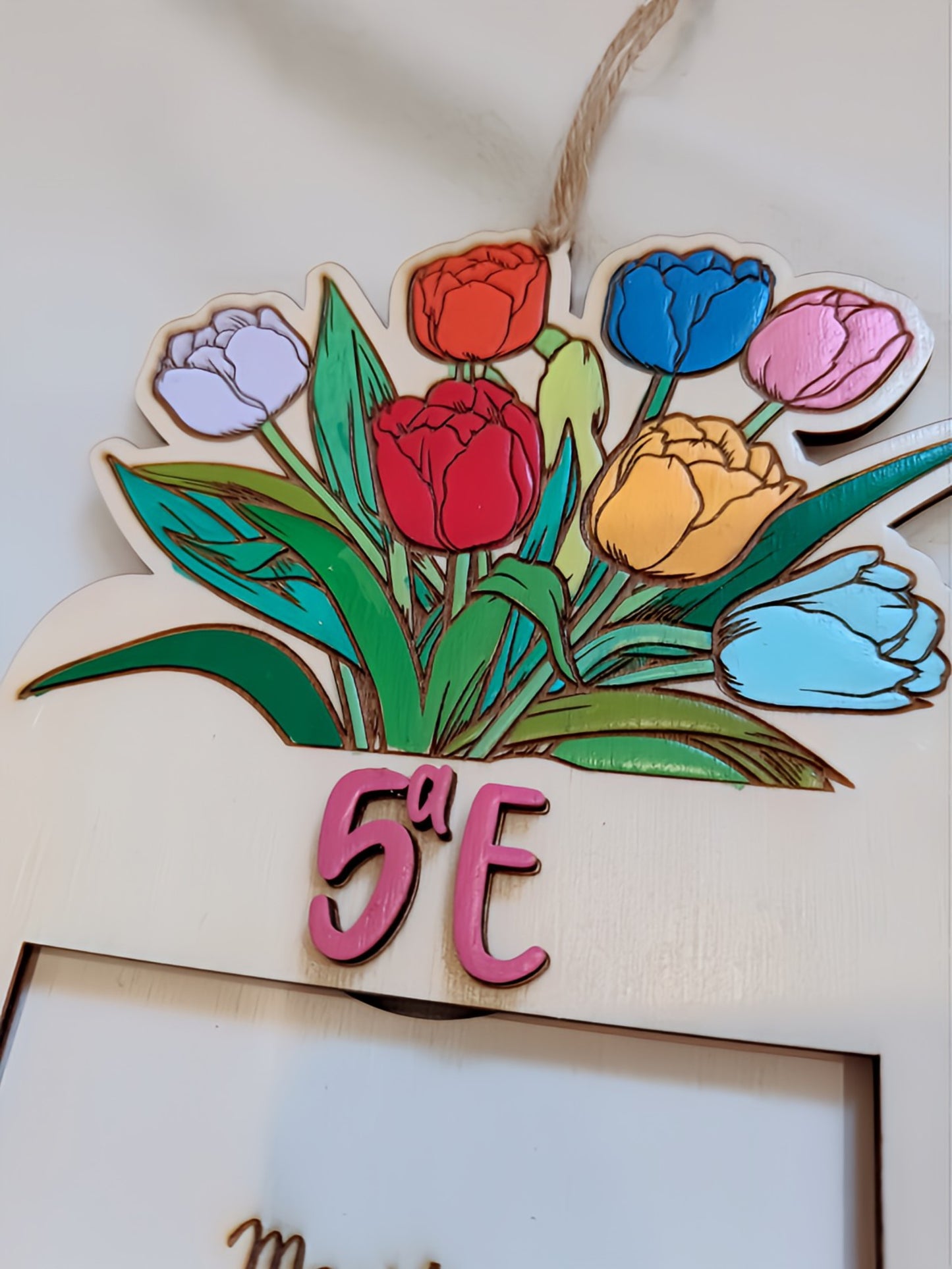 Wooden hanging sign with colorful tulips and pink 5ª E text on white background