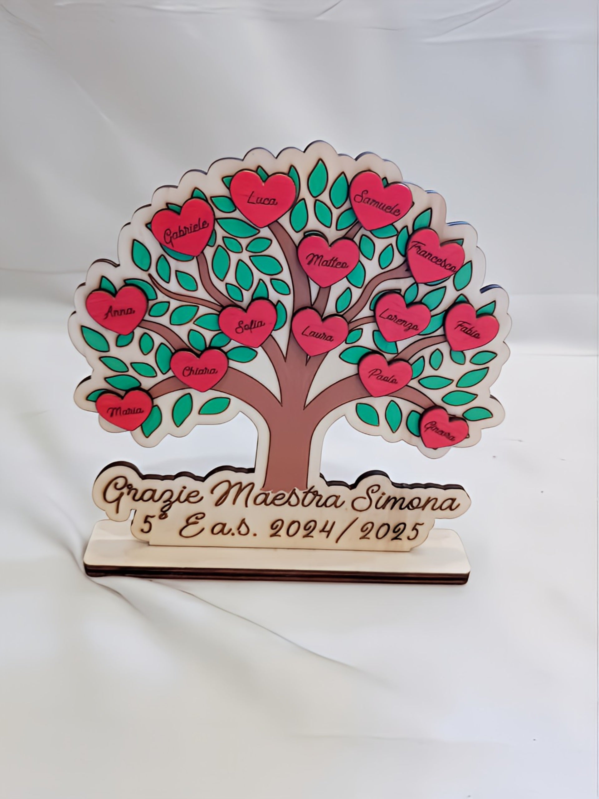 Albero della classe in legno fatto a mano con tronco dipinto marrone, foglie verde acqua e cuori rossi con i nomi dei bambini incisi a pirografia. Base personalizzata con la scritta "Grazie Maestra Simona 5° E a.s. 2024/2025". Regalo di fine anno per insegnante.