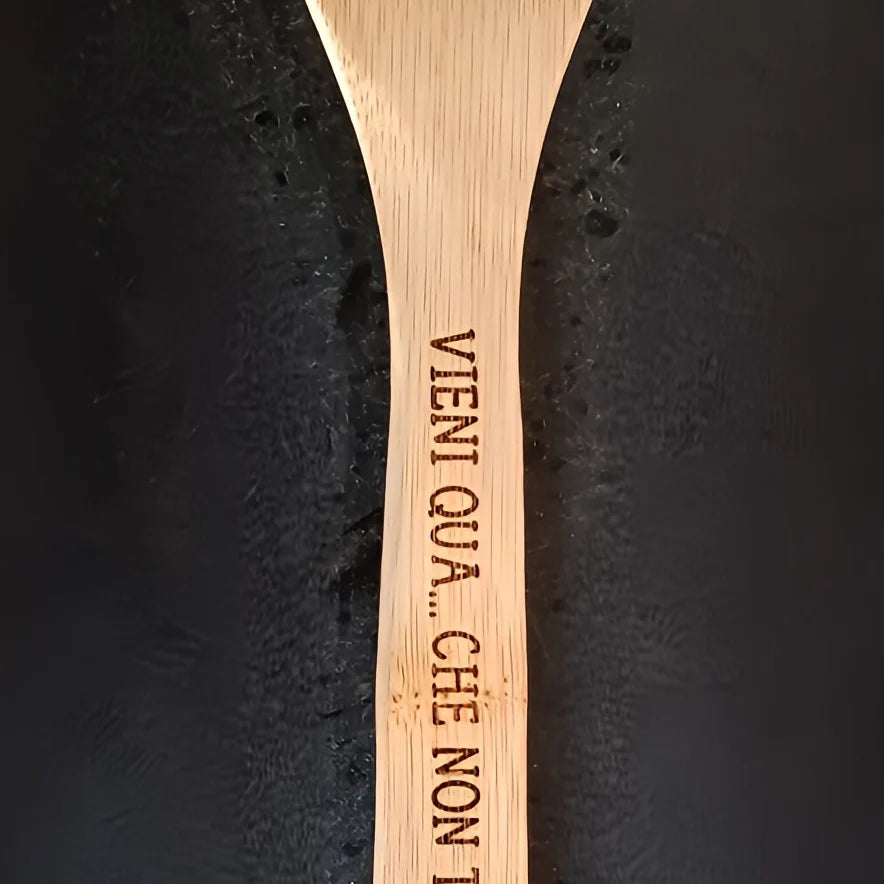 Wooden spoon engraved with Italian phrase VIENI QUA on black background
