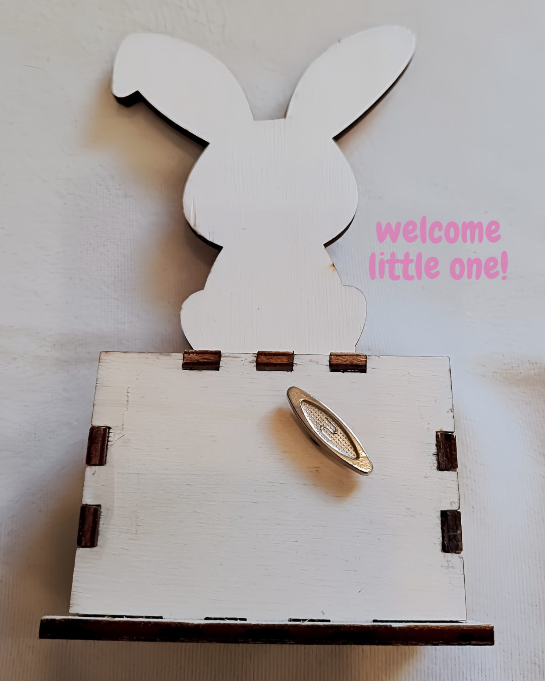 White wooden bunny box with silver handle and pink 'welcome little one!' text